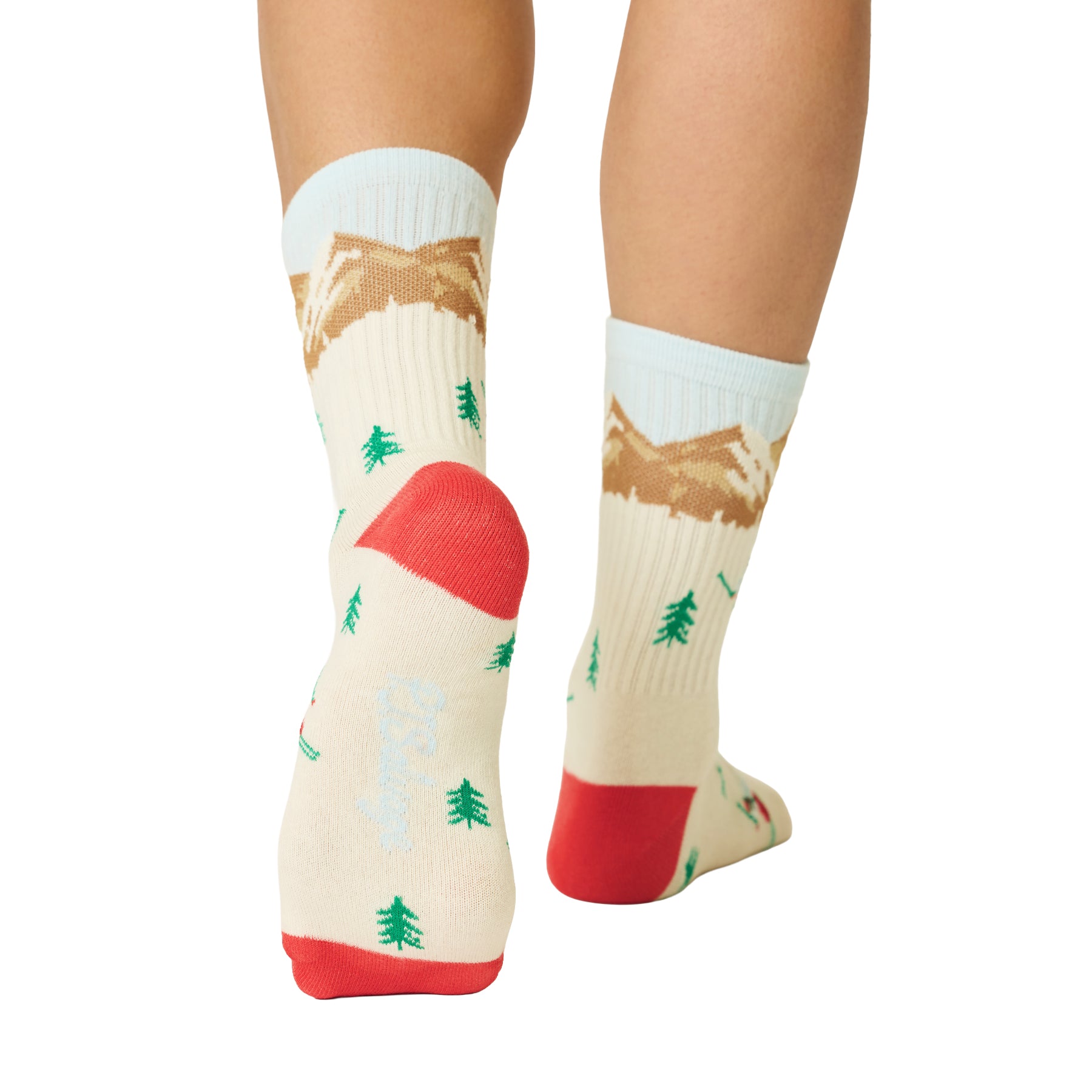 Ivory crew socks with a winter ski print, featuring brown mountains, green pine trees, red accents and light blue cuffs.
