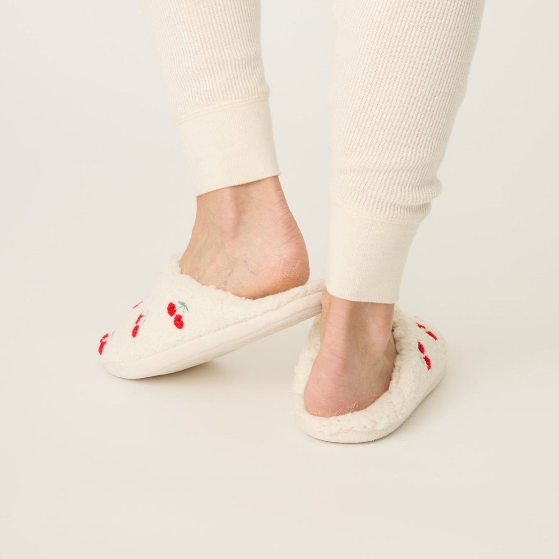 Fuzzy and fleecy slippers in ivory with red cherry print, rear view.