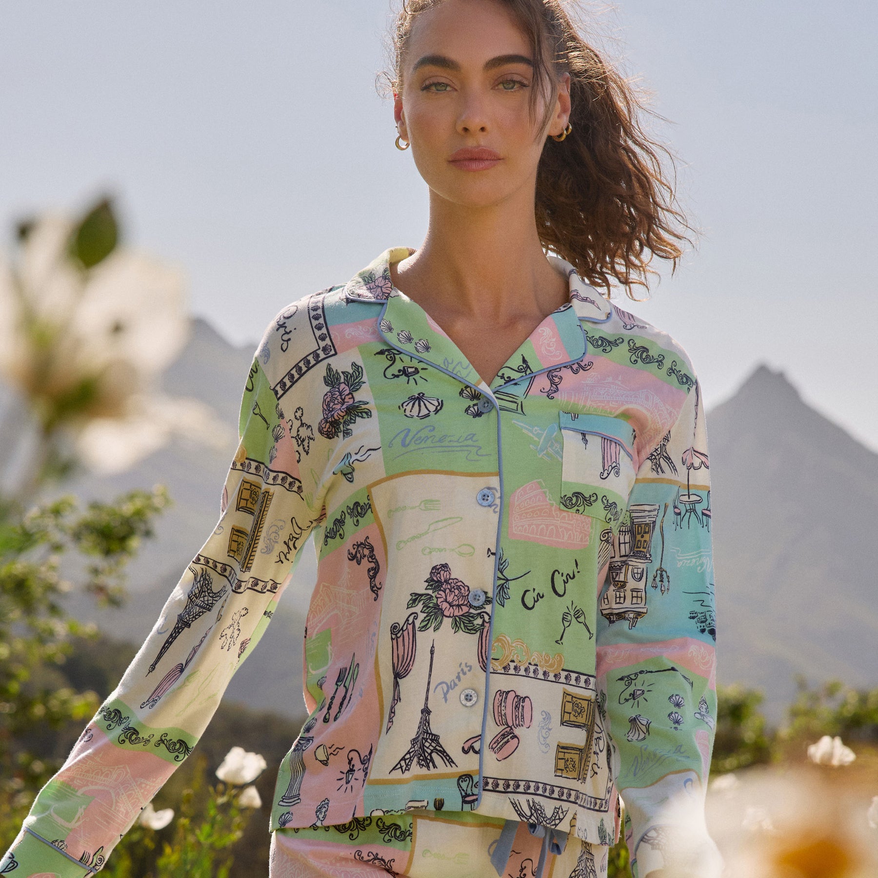 Close-up of the pyjama top showing the pastel Paris-inspired print with illustrated landmarks, cafés, and travel motifs, worn outdoors.