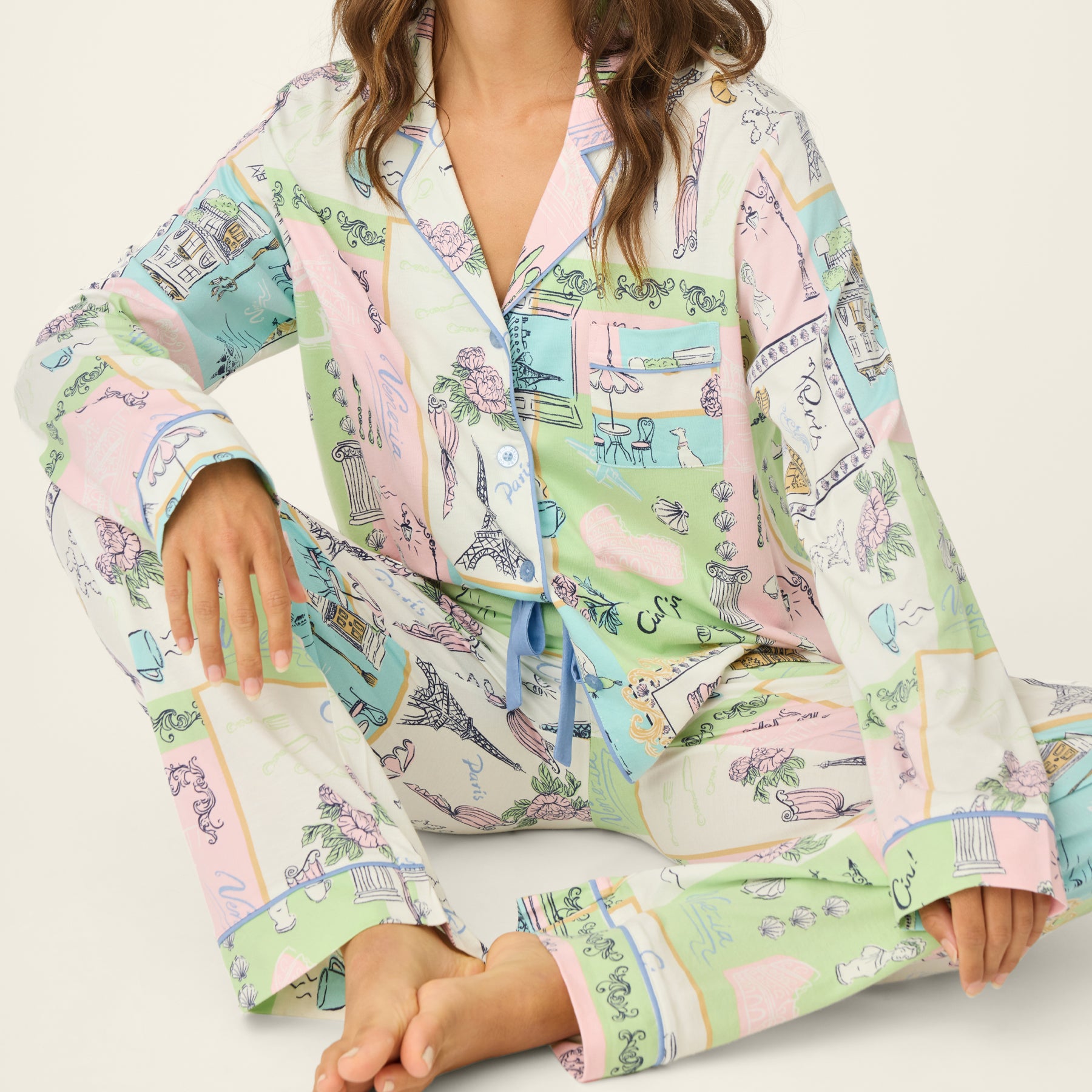 Model seated wearing the pastel printed pyjama set, showing the button-front top, cuffed sleeves, and drawstring waist pants.