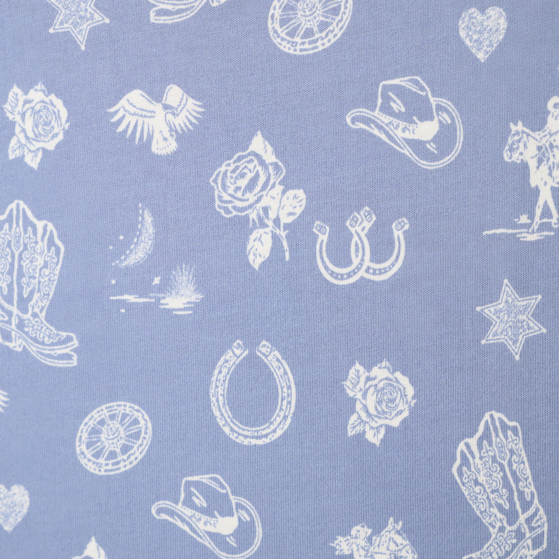 Close-up of light blue pyjama fabric with white western motifs including boots, hats, and horseshoes