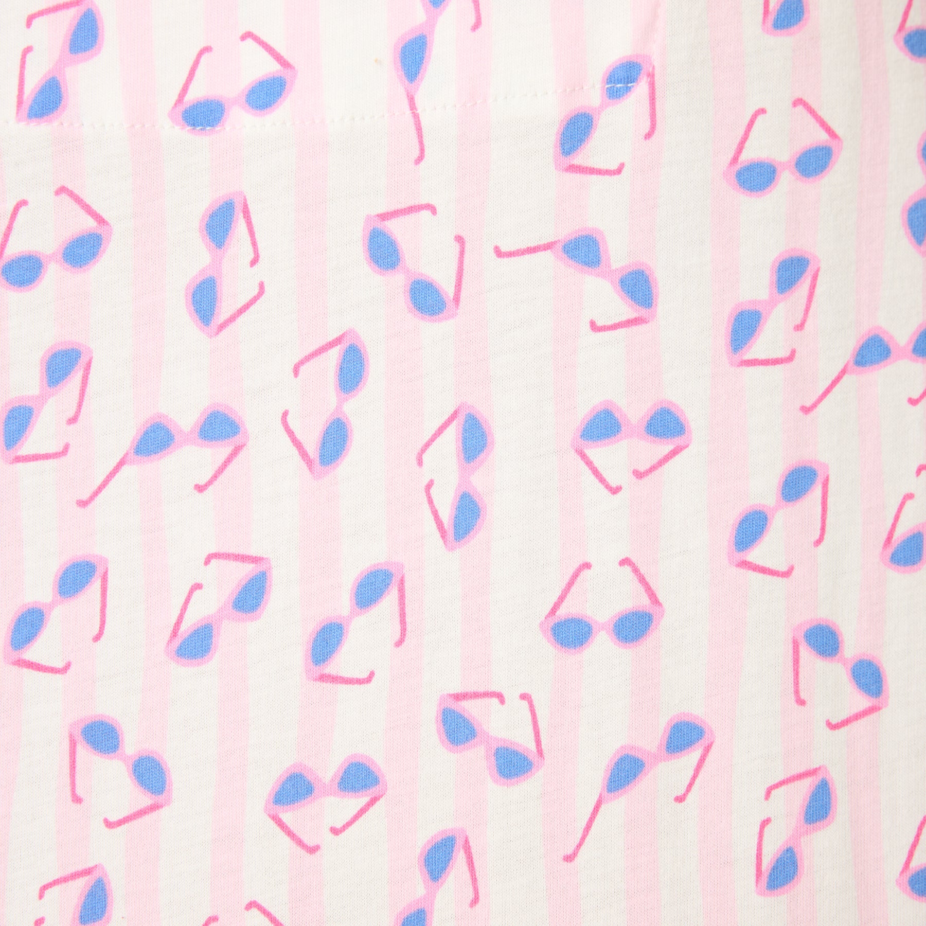 Close-up of light pink striped fabric with blue and pink sunglasses print detail