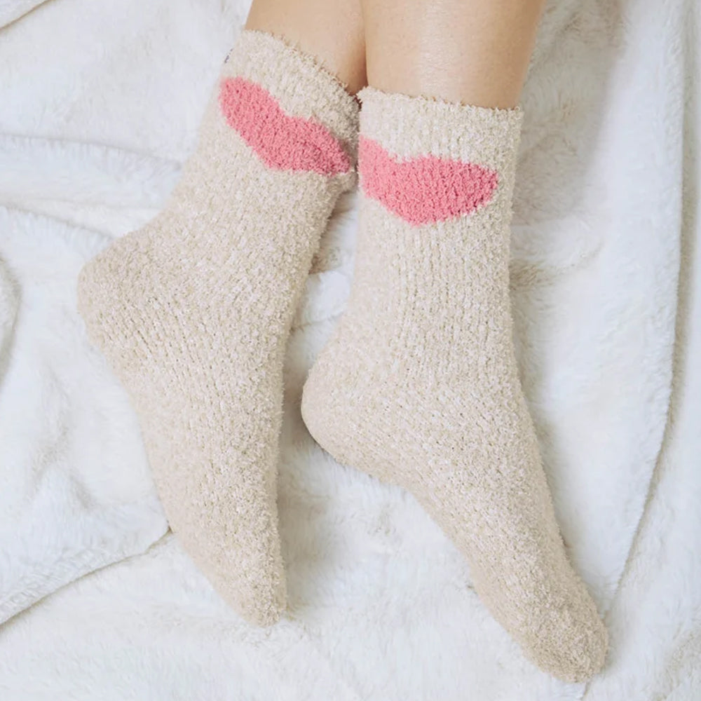 Model wearing Splendid cozy oatmeal-coloured crew socks with pink heart designs near the cuffs, resting her feet on a soft white blanket.