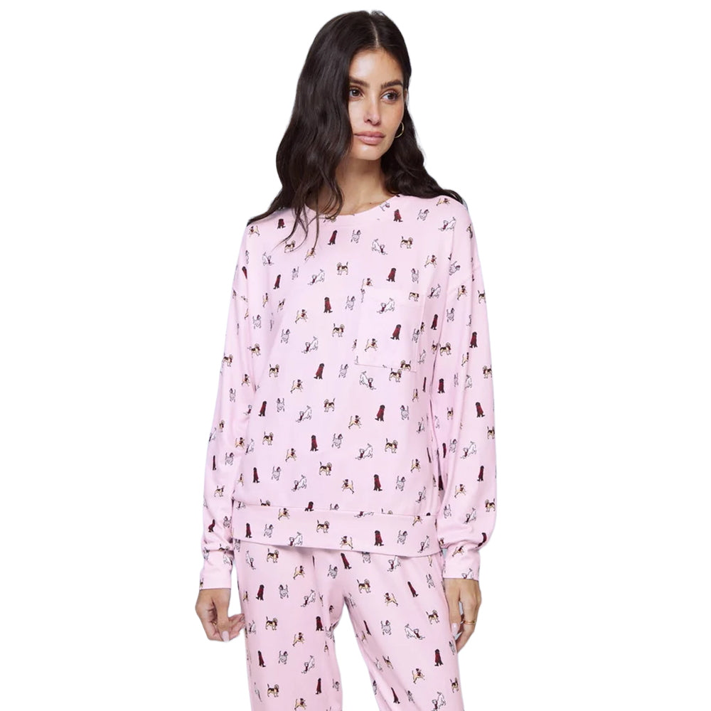 Model wearing Splendid  Cozy Canines light pink pajama set featuring a relaxed crewneck sweatshirt with dropped shoulders, long sleeves, and playful multicoloured dog illustrations.