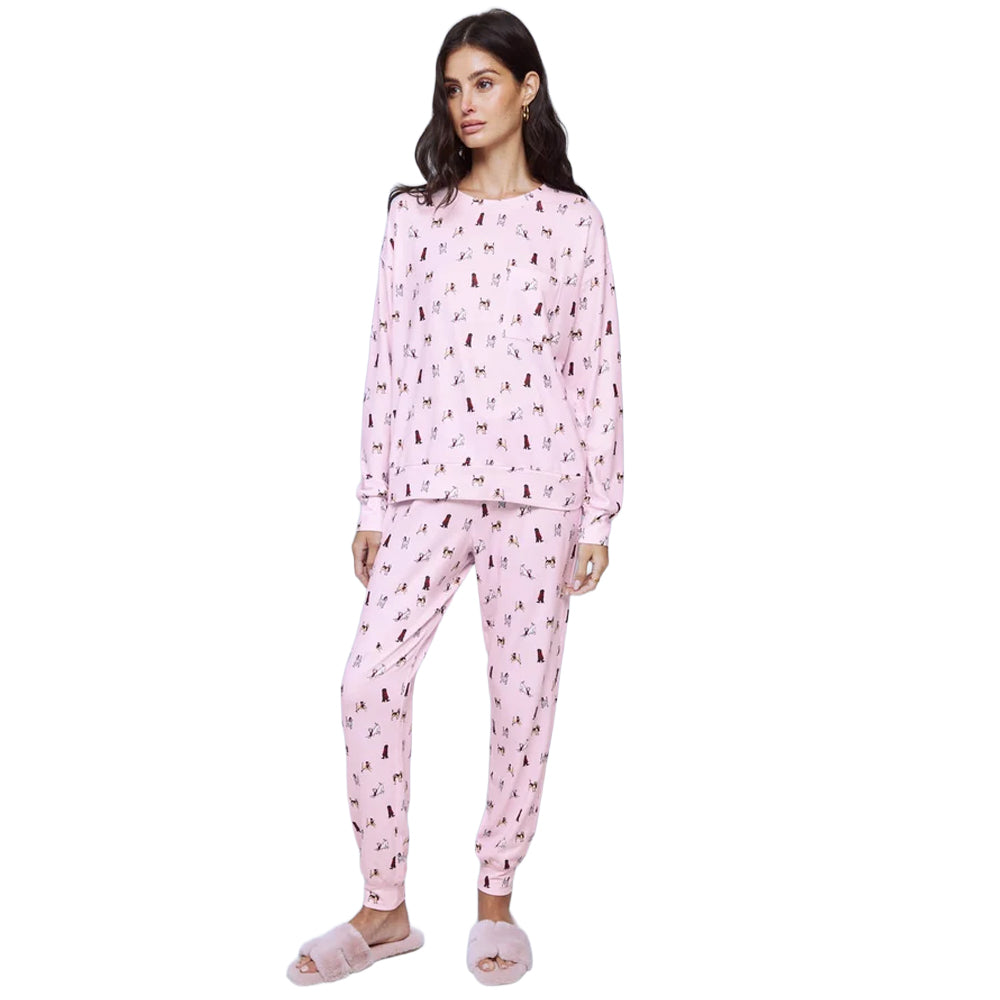 Model wearing Splendid Cozy Canines pink pajama set featuring a relaxed long-sleeve crewneck top and matching tapered jogger pants with ribbed cuffs and an all-over dog print.