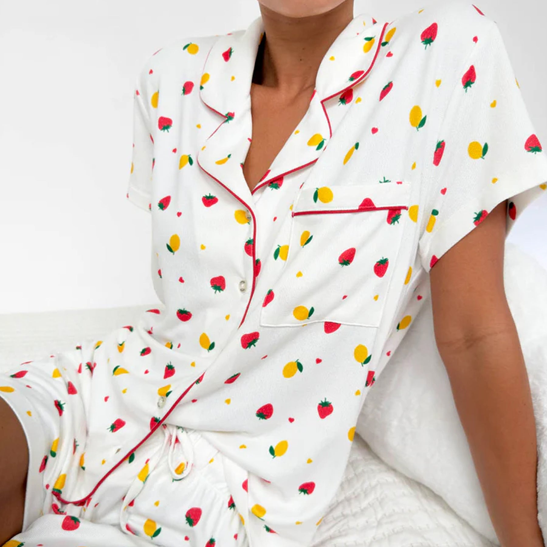 Woman wearing white short sleeve pyjama set with strawberry and lemon print and red piping detail