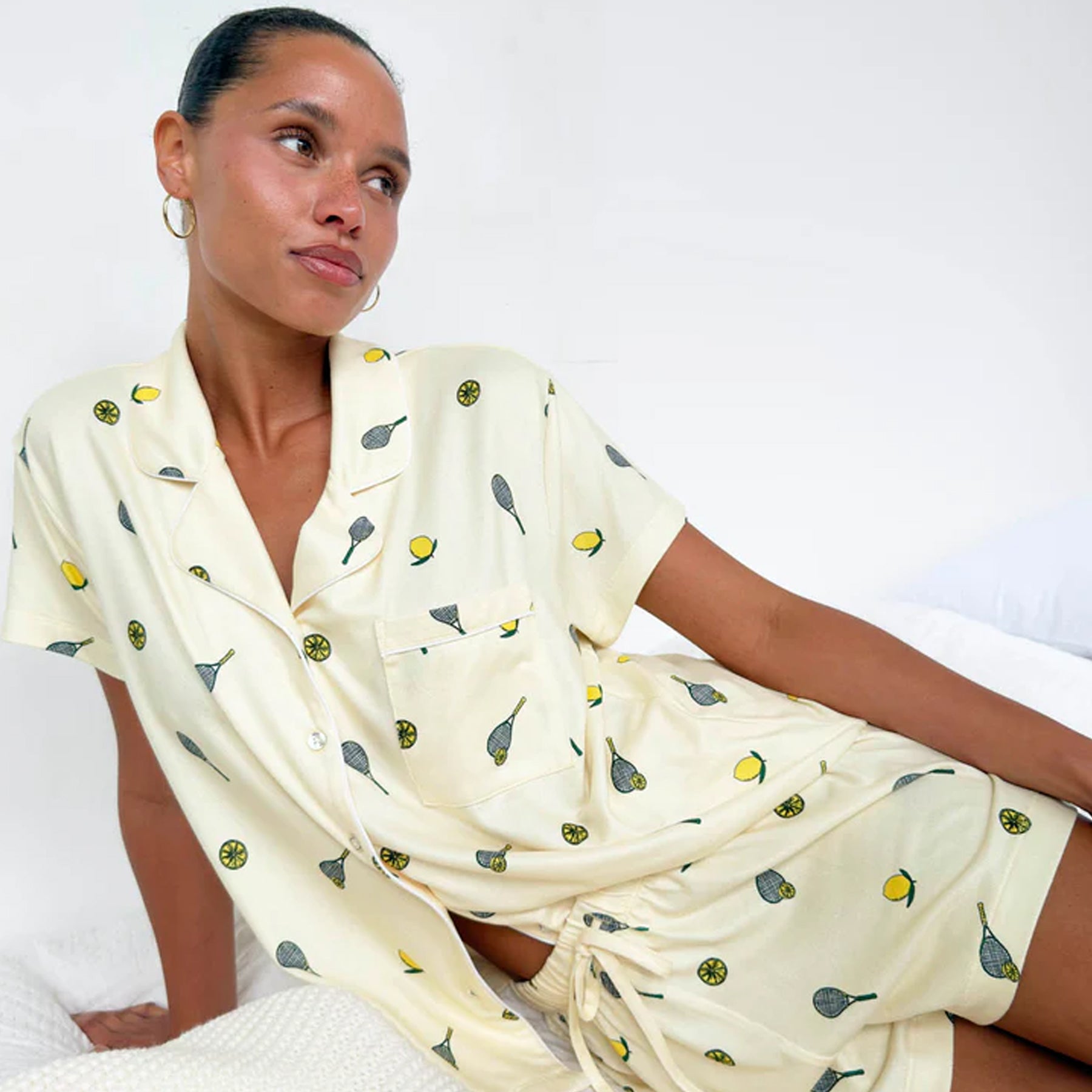 Woman lounging in pale yellow short sleeve pyjama set with lemon and tennis racket print