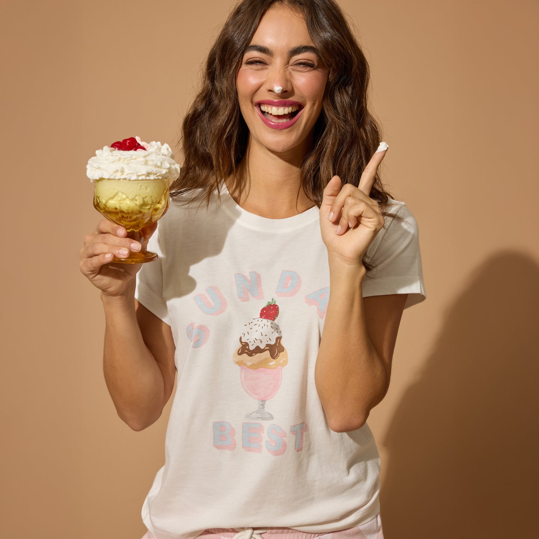Woman holding a dessert and pointing upwards, wearing a t-shirt with ice cream graphics.