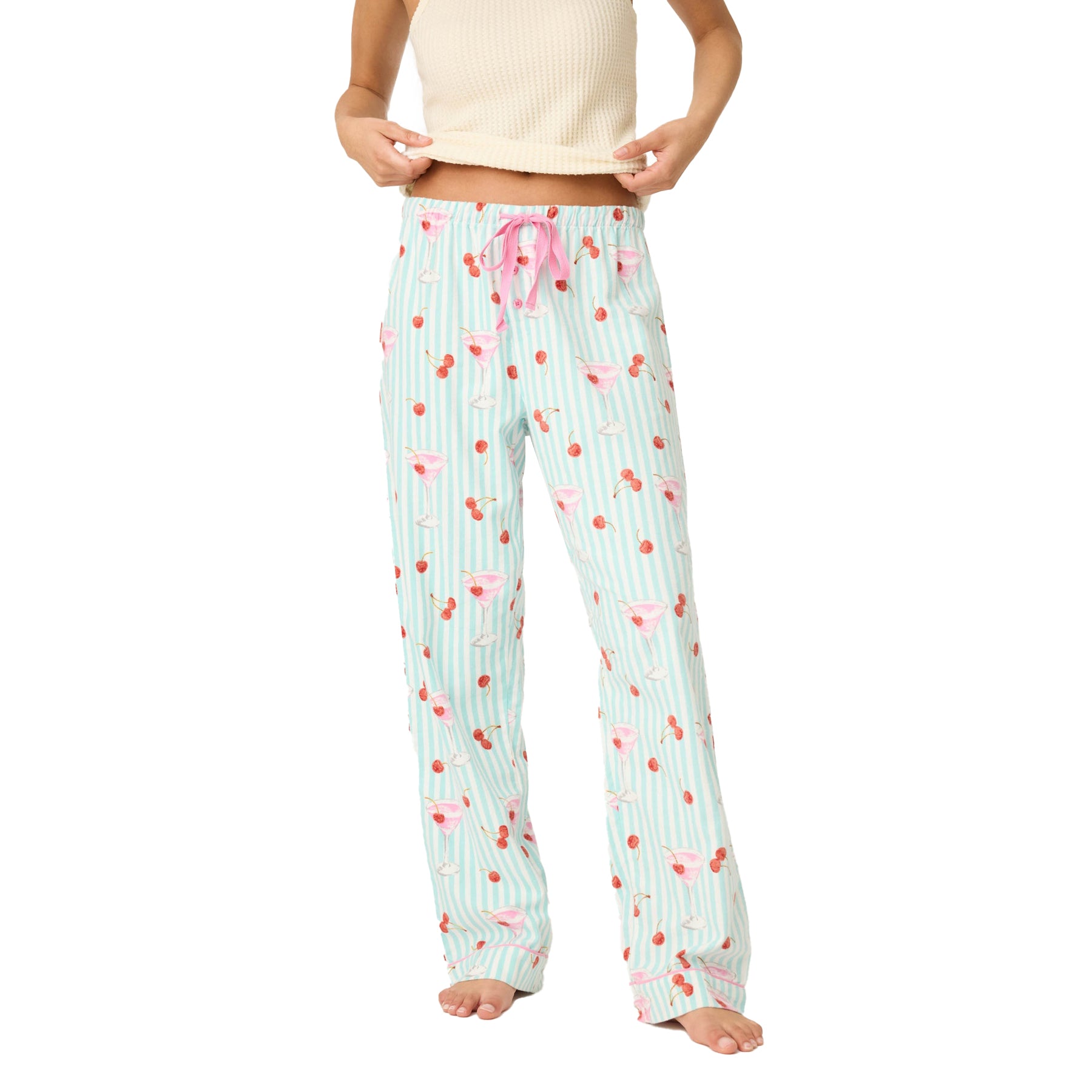 Woman wearing mint green striped pajama pants with pink cocktail and cherry print, styled with a cream top.