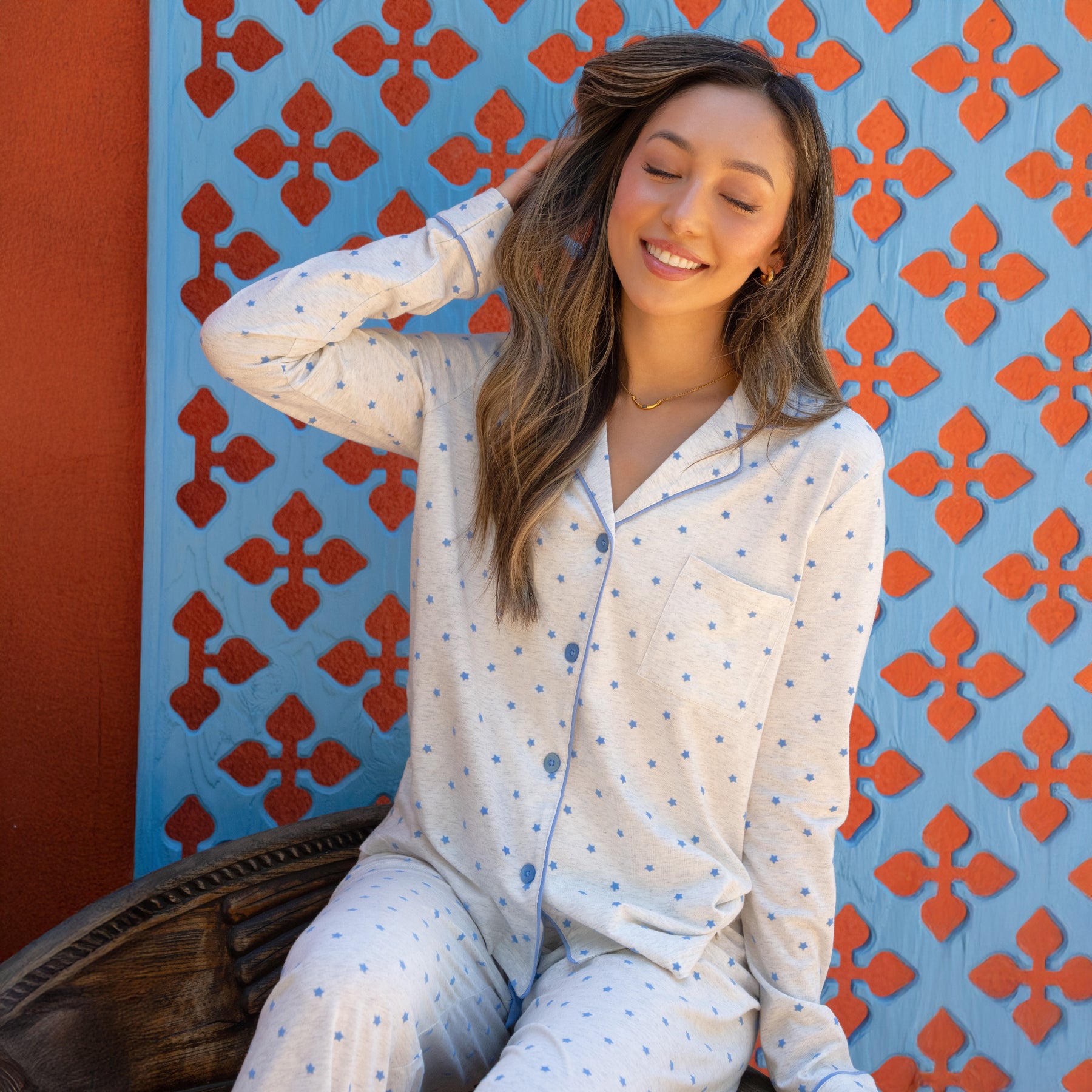 Woman in a white polka dot shirt sitting against a colorful wall with red geometric patterns.