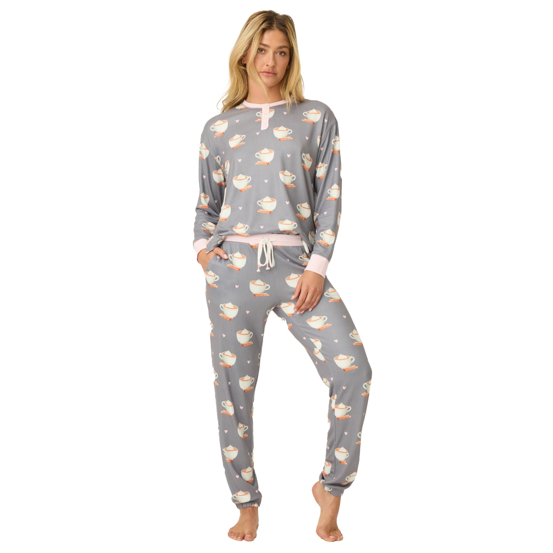 Woman wearing grey pajama set with cocoa mug print and pink trim.