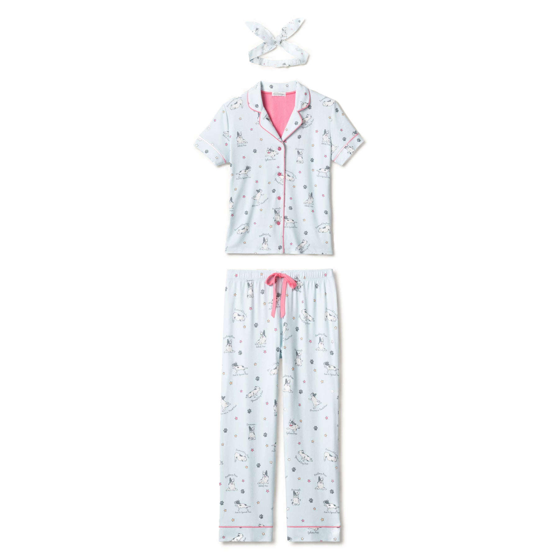 Flat lay of a matching light blue pyjama set featuring a short-sleeve button-up top, drawstring pants, and a headband, all with playful dog yoga pose illustrations and pink piping.