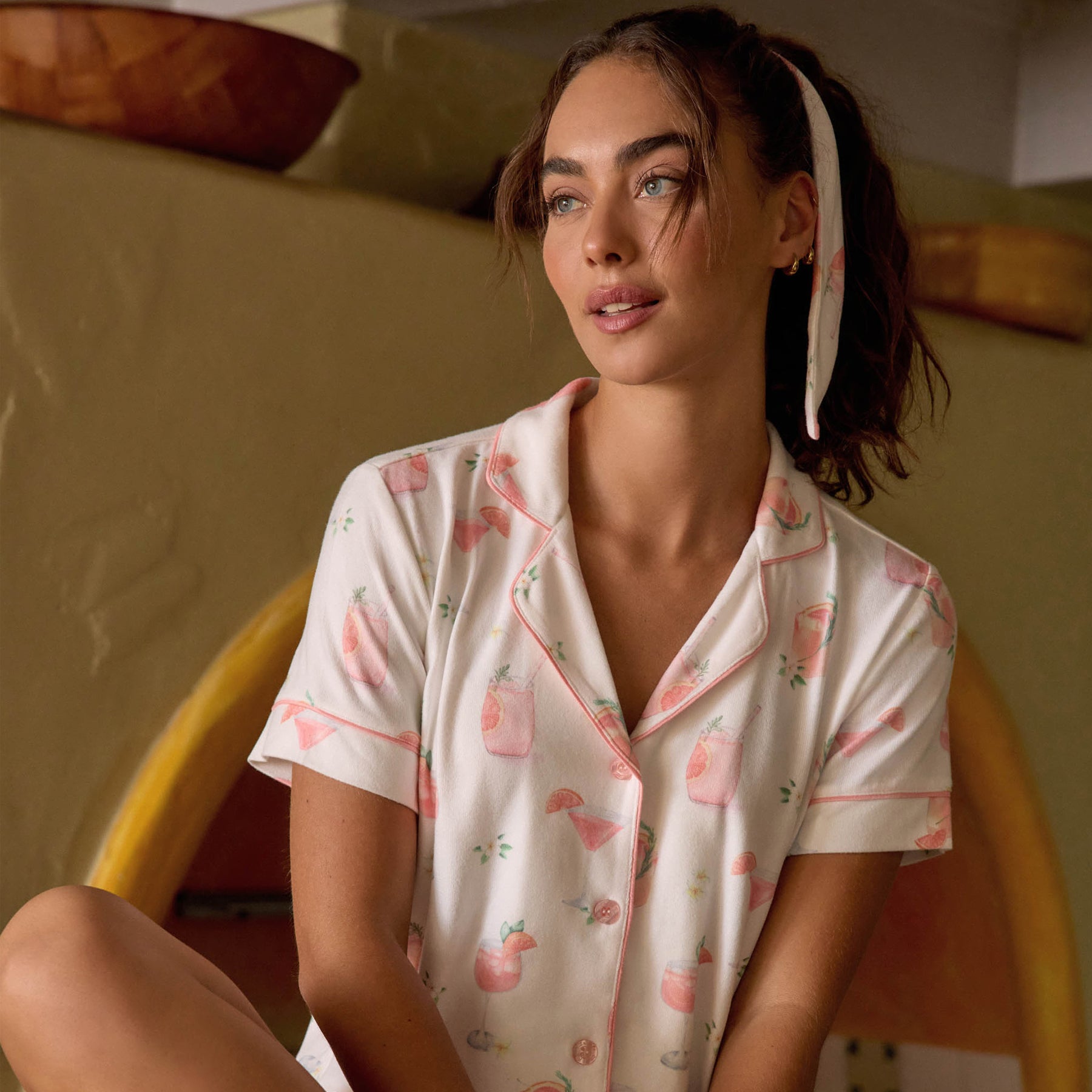 Lifestyle image of woman wearing ivory cocktail-print pyjamas in a warm-toned interior setting