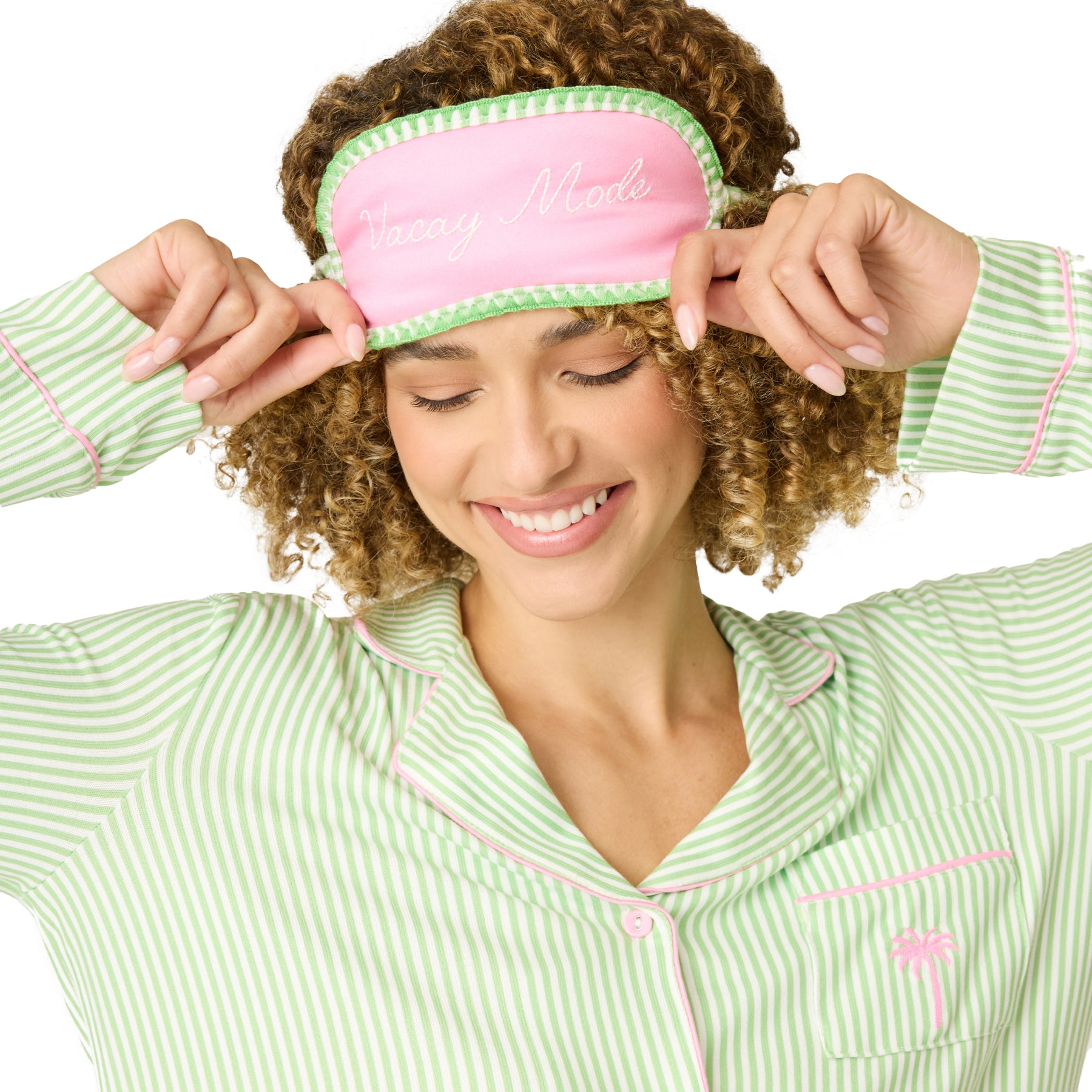Close-up of pink “Vacay Mode” sleep mask with green trim worn with striped pyjama set