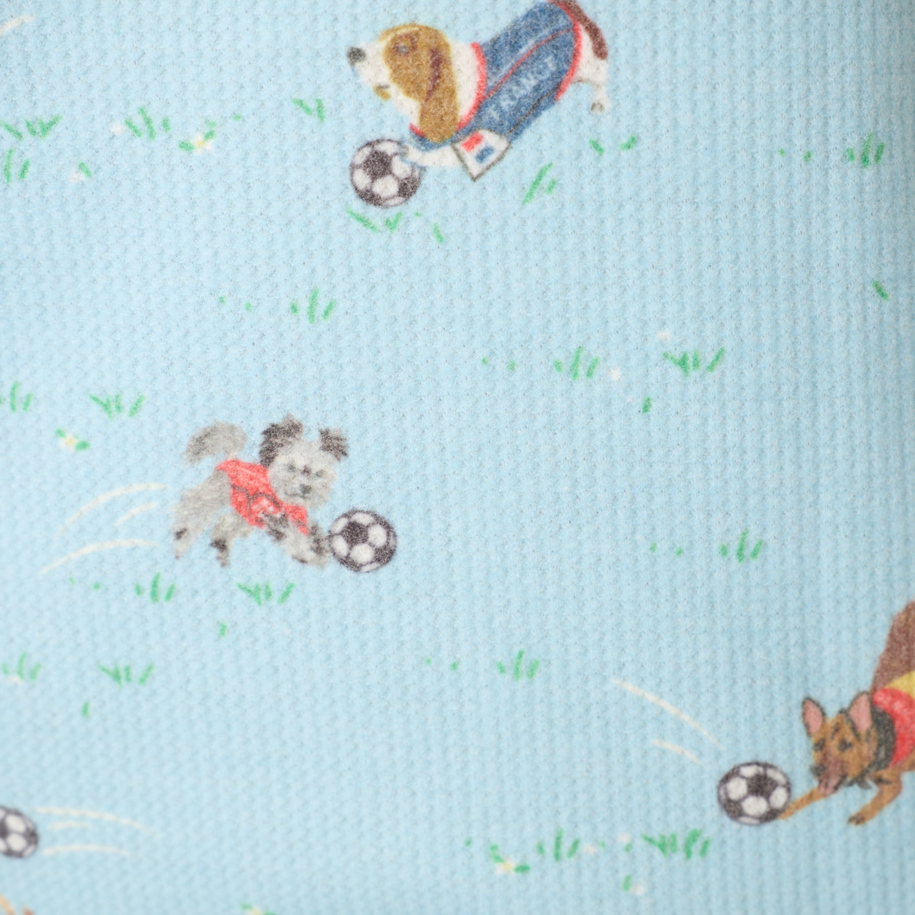 Detailed fabric close-up of blue pajama set with playful dogs and soccer balls print on textured material