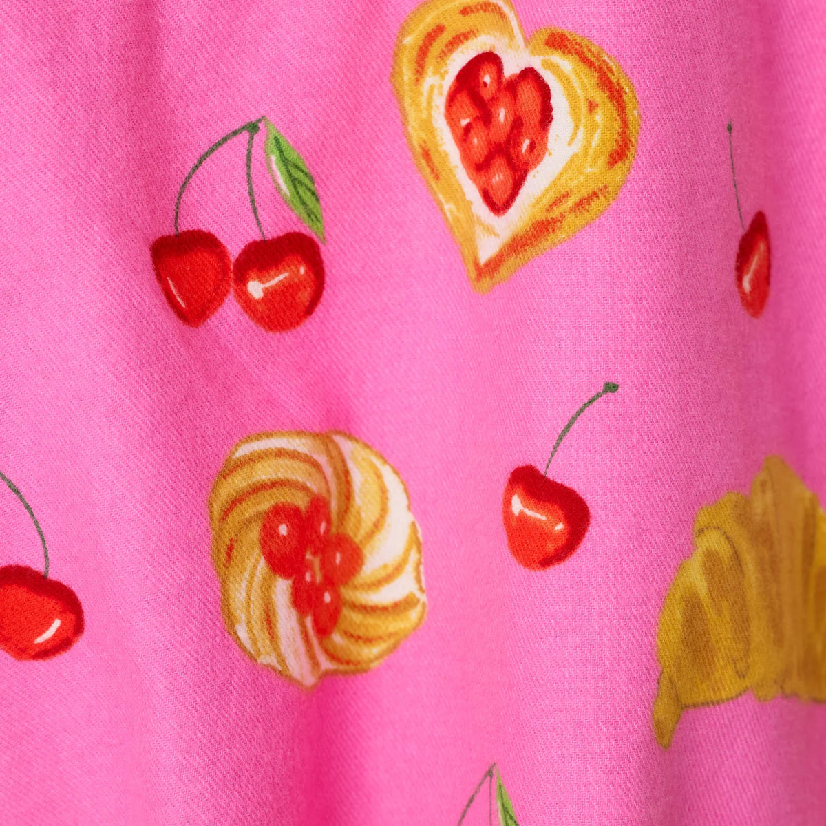 Close-up of pink sleepwear fabric featuring colorful cherries, croissants and heart-shaped pastry illustrations.