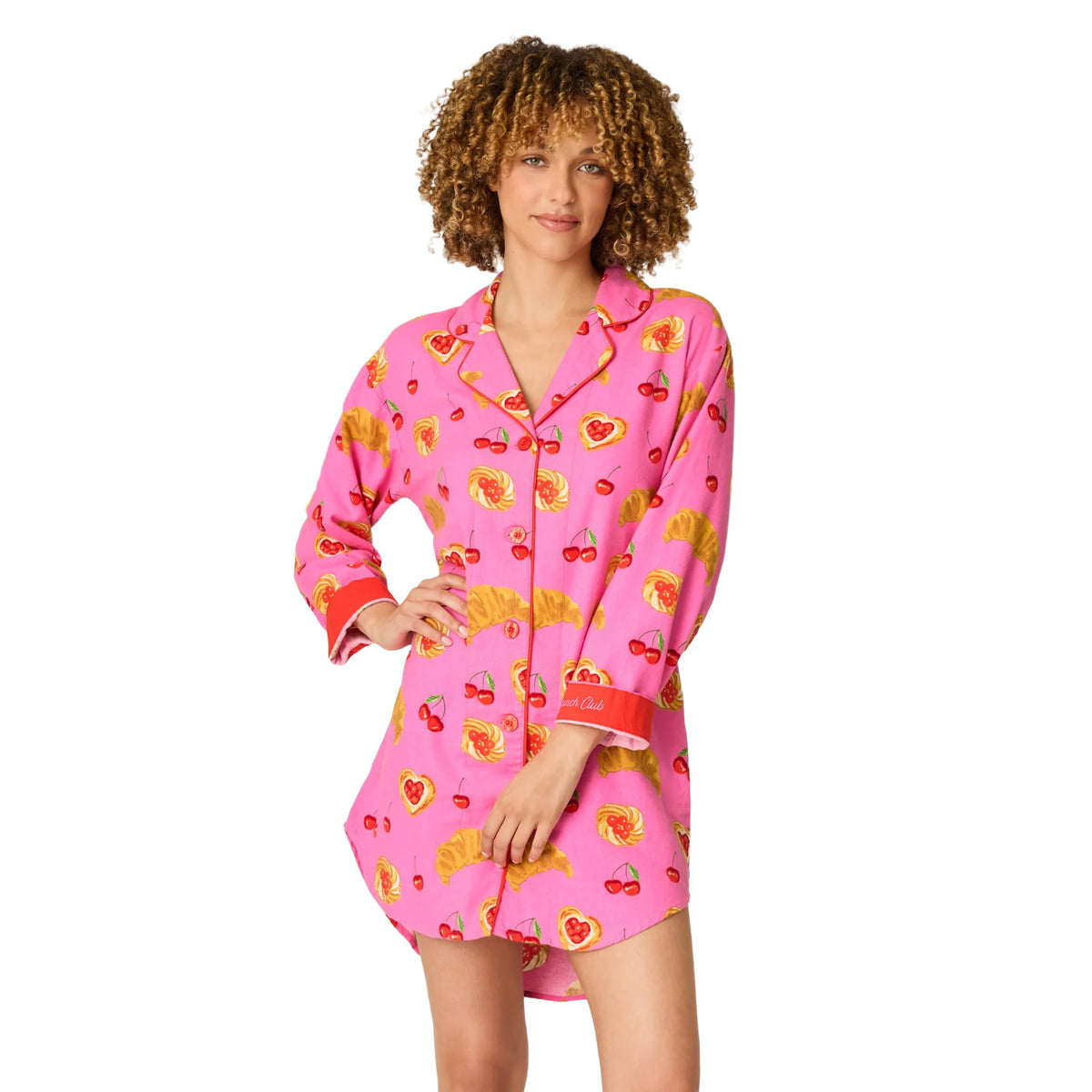 A woman modeling a pink long-sleeve pajama shirt with a fruit print, featuring cherries, strawberries, and citrus slices, set against a plain white background.