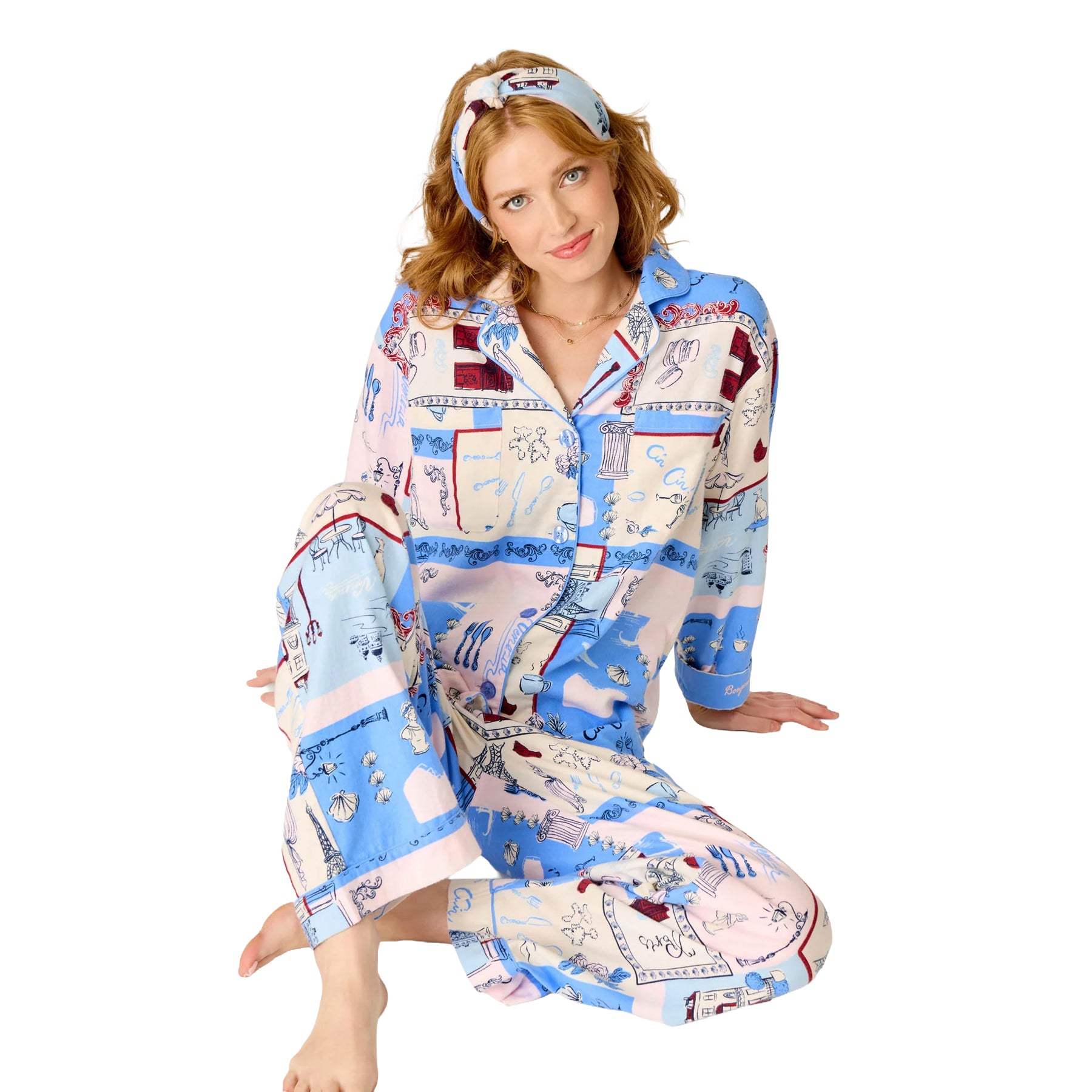 Woman seated in a blue, blush and cream printed pajama set featuring Parisian illustrations and a matching headband.
