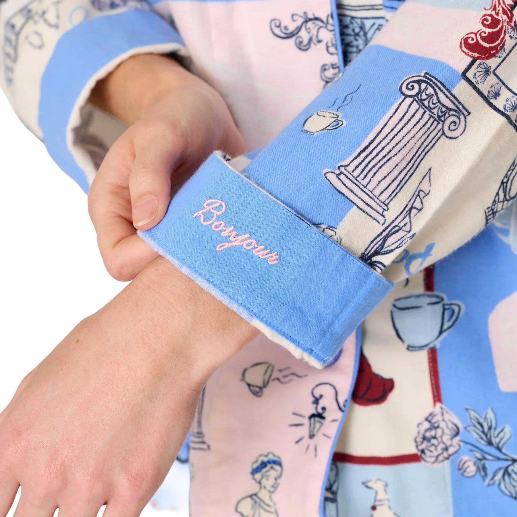 Close-up of blue pajama cuff embroidered with “Bonjour” in pale pink, surrounded by Paris-inspired illustrations.