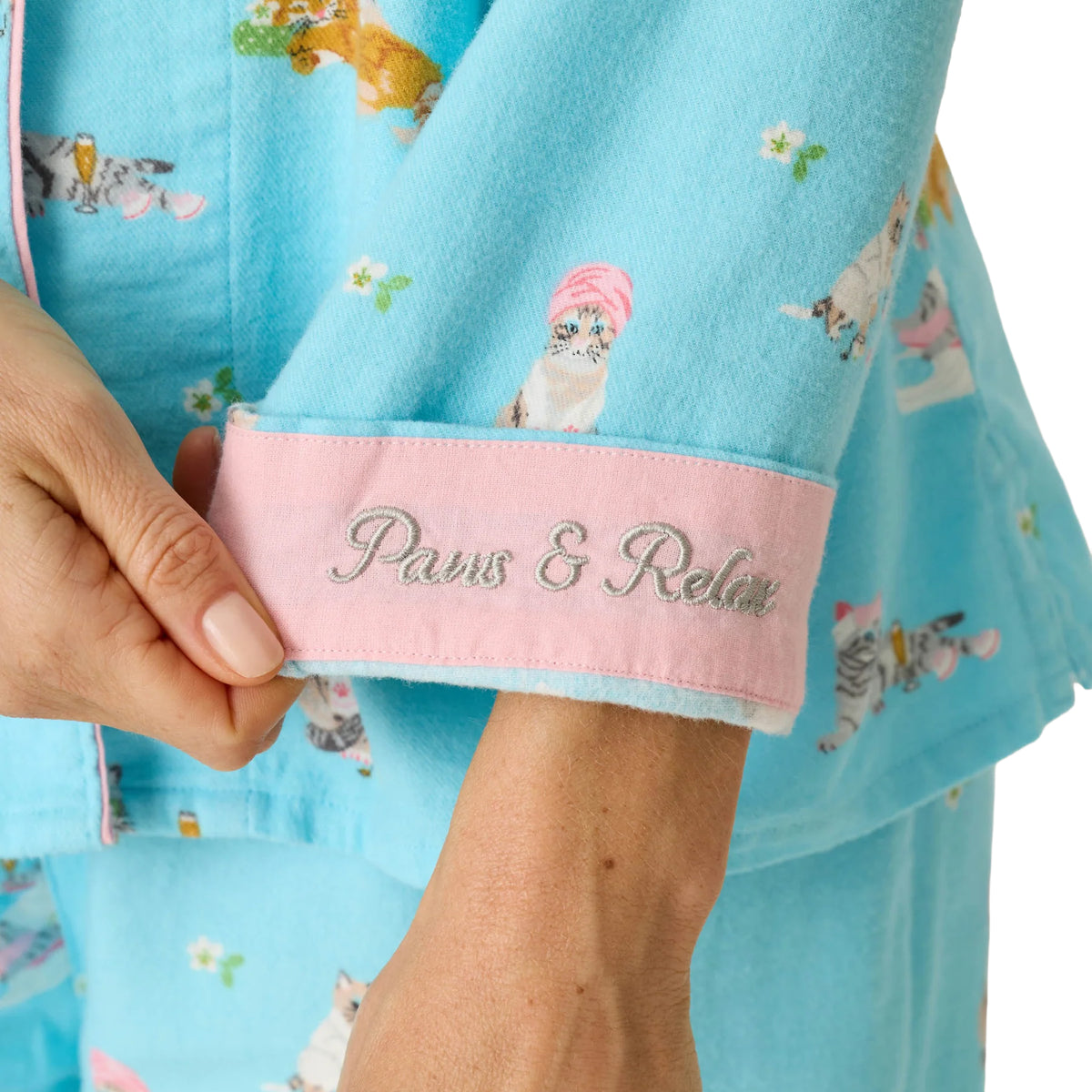 Close-up of PJ Salvage Paws & Relax flannel pyjama sleeve featuring pink cuff with embroidered Paws & Relax lettering and playful cat print.