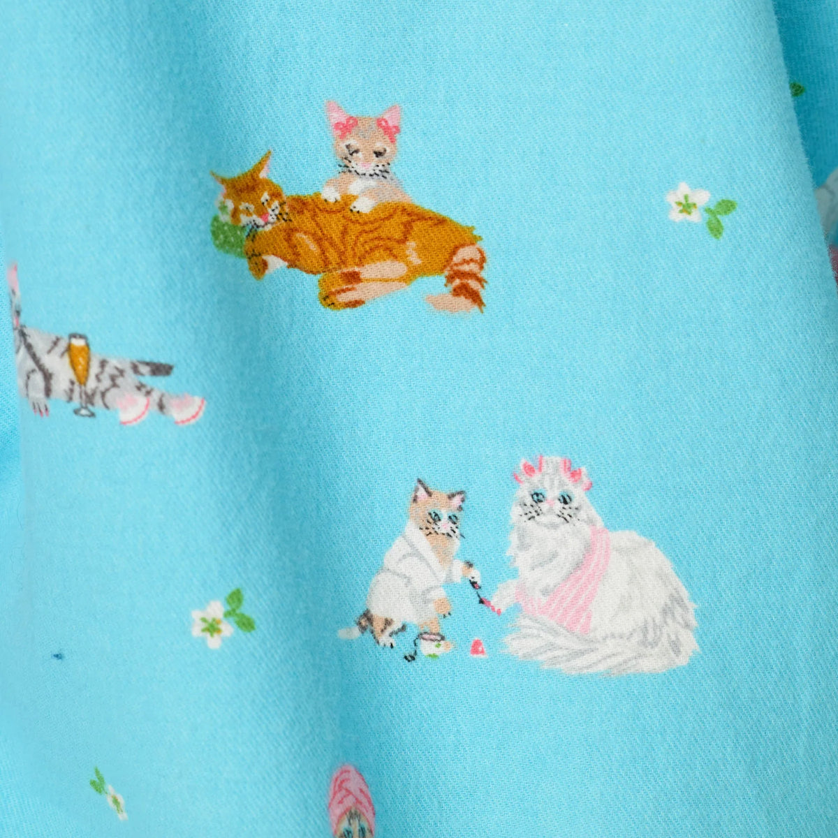 Close-up of PJ Salvage Paws & Relax flannel fabric featuring playful cats in pink accessories, orange kittens and small floral details on a bright blue background.