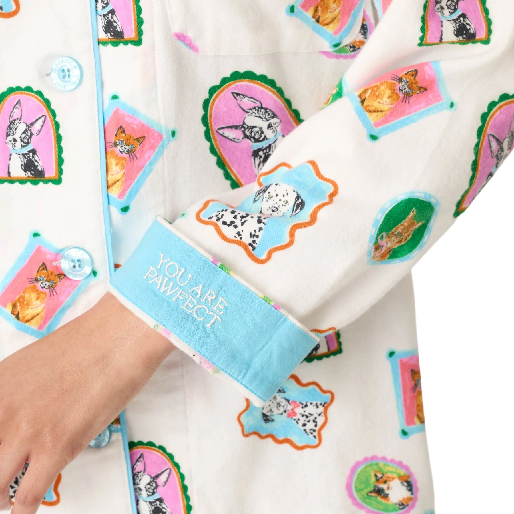 Close-up of cream pajama top featuring colorful framed dog and cat print, blue piping and “You Are Pawfect” embroidered cuff.