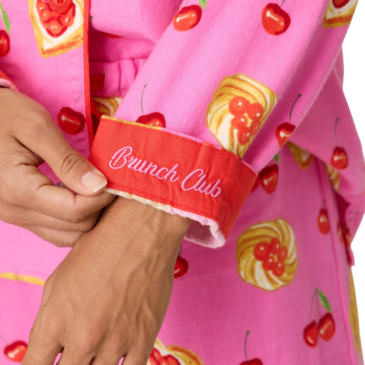 Close-up of pink pajama sleeve featuring cherry and pastry print with red cuff embroidered “Brunch Club.”