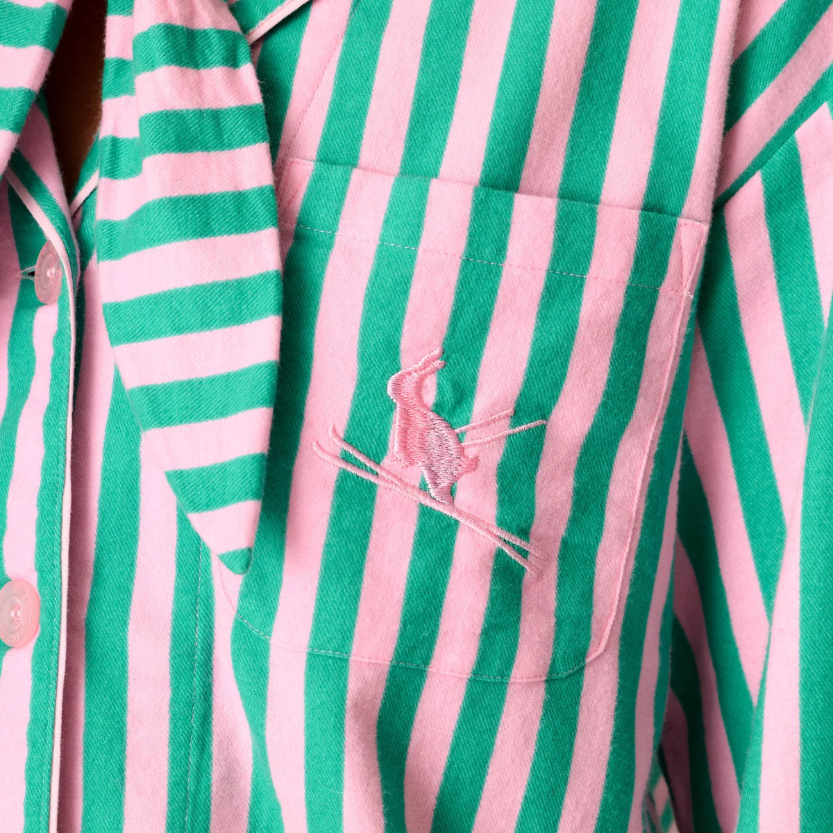 Close-up of pink embroidered bunny detail on chest pocket of pink and green striped flannel pajama top.