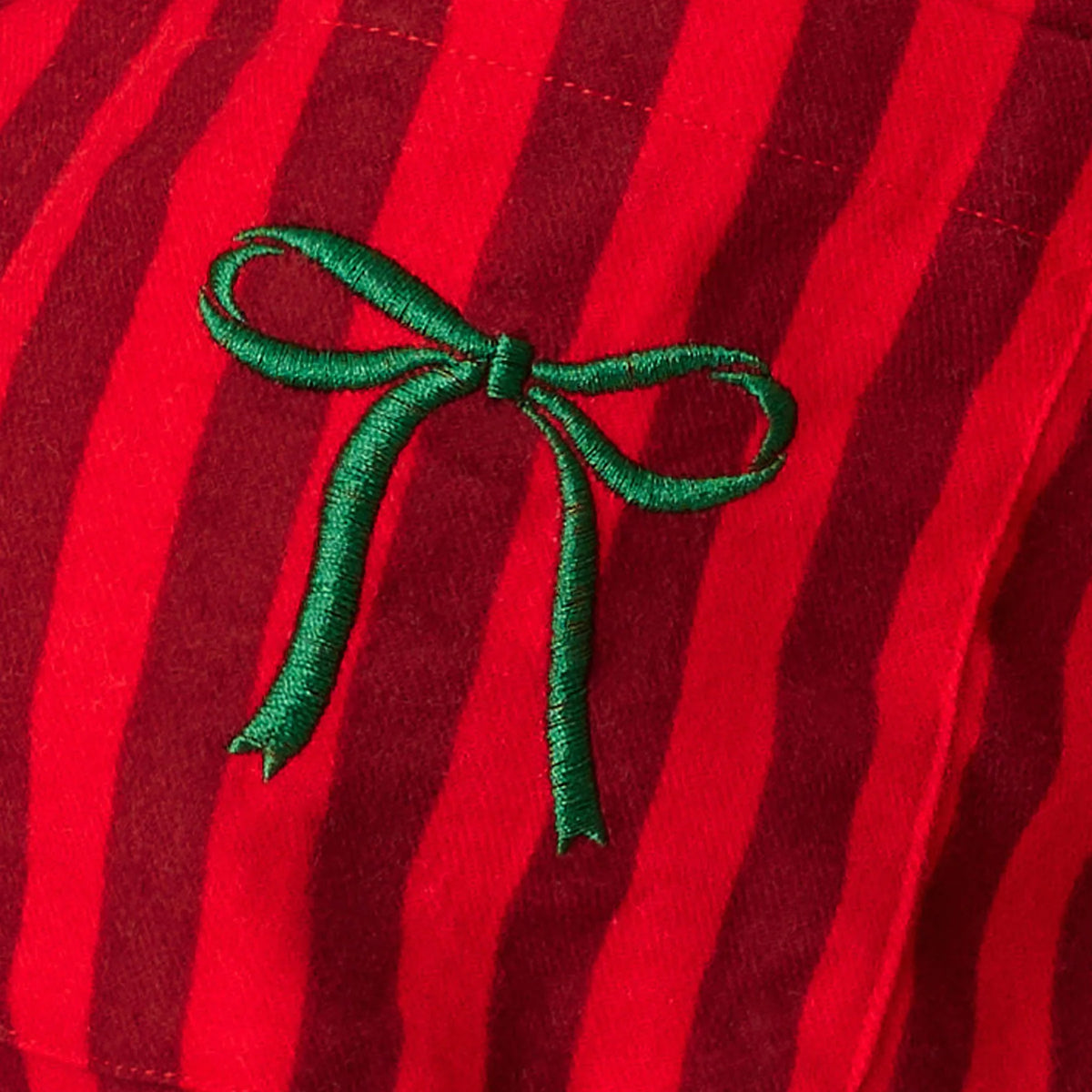 Close-up of green embroidered bow detail on red and burgundy striped flannel pajama chest pocket.