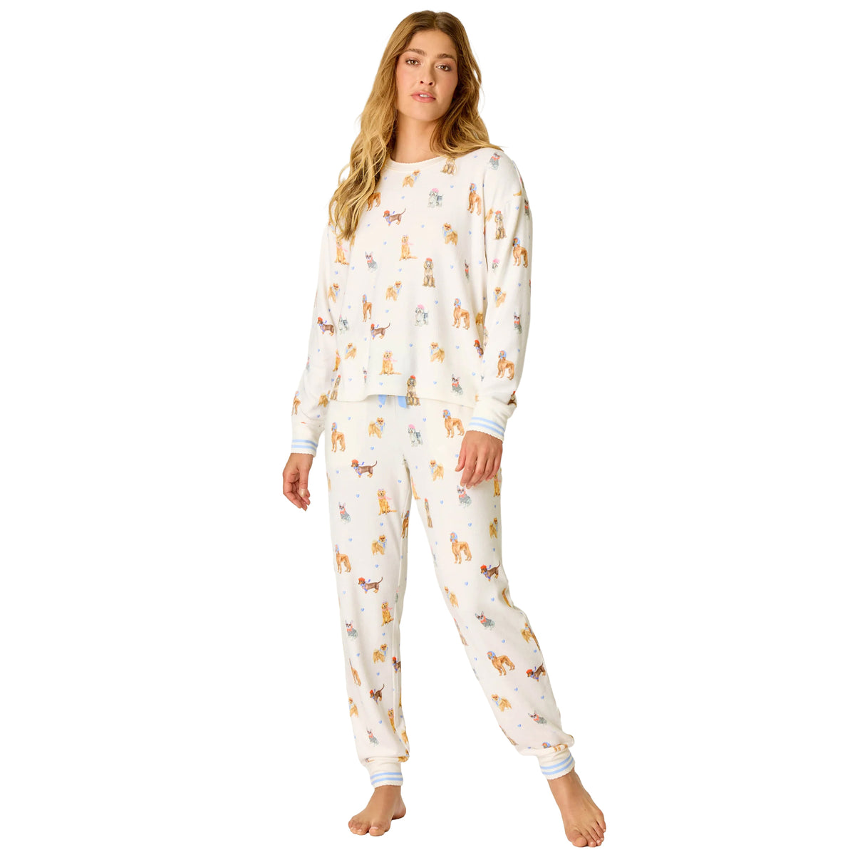 Woman wearing an ivory long-sleeve pajama set with a playful French dog print, blue heart accents and striped cuffs.
