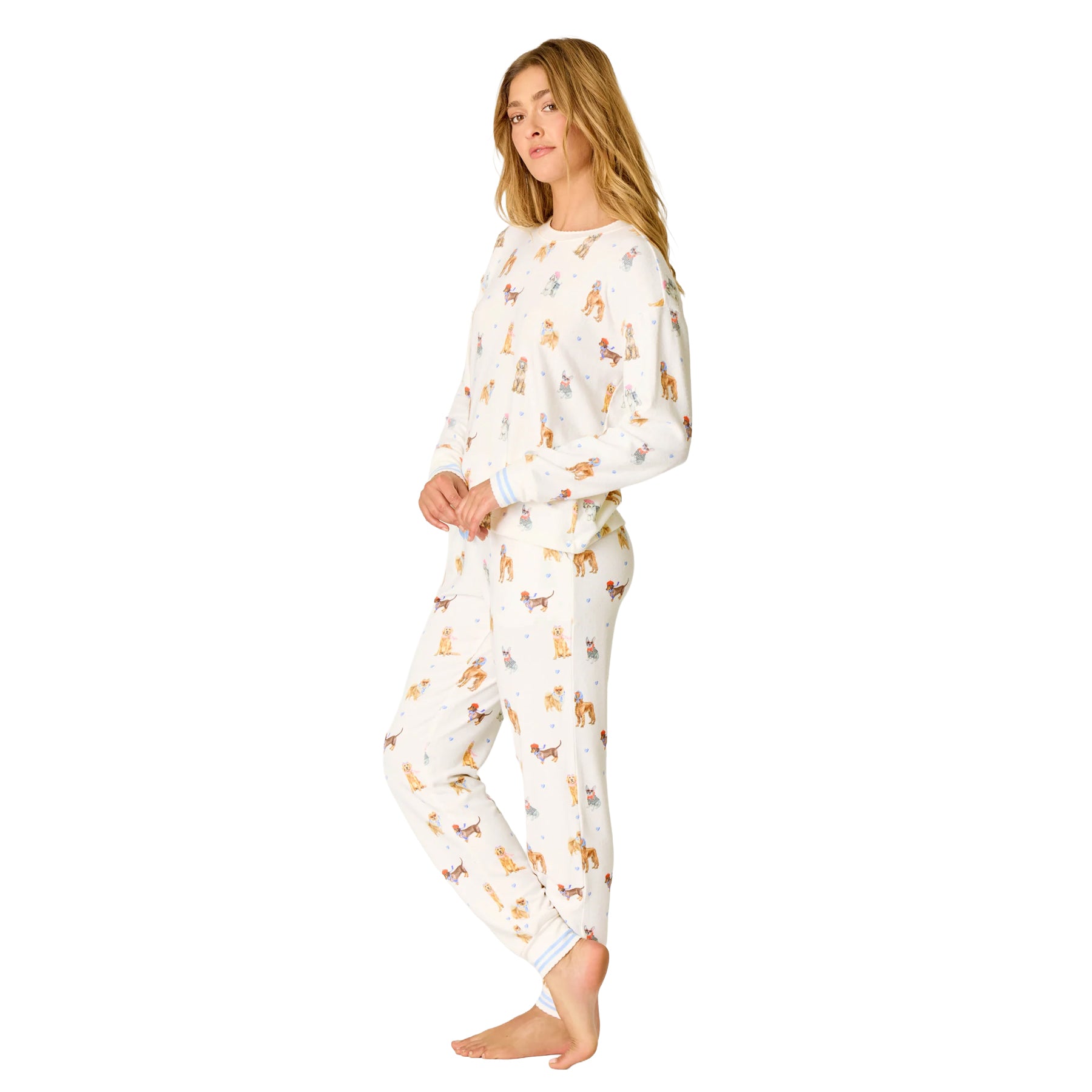 Woman wearing an ivory pajama set covered in colourful illustrated dogs, finished with soft blue striped cuffs.