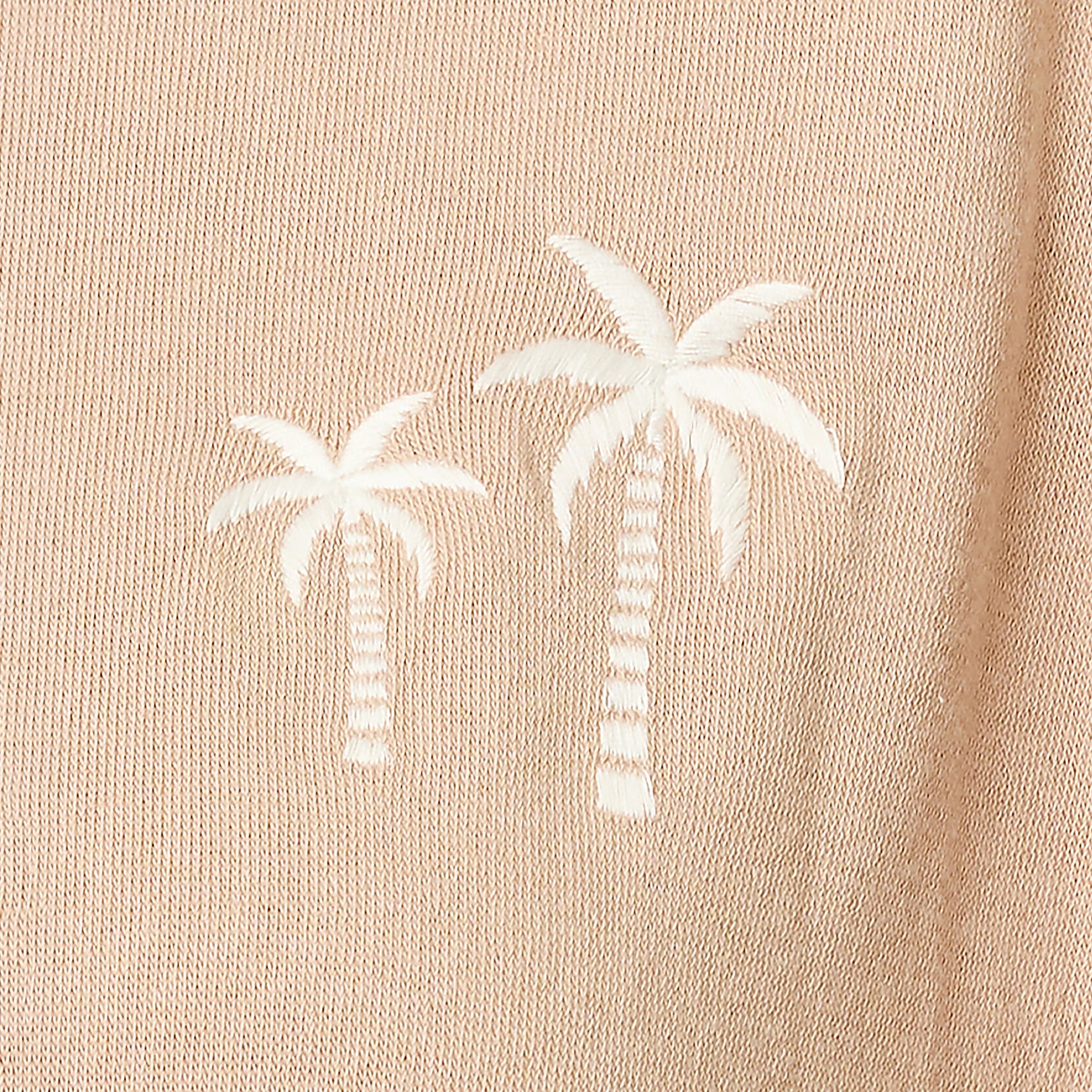 Close-up of embroidered white palm tree detail on a warm taupe lounge sweatshirt made from soft knit fabric.
