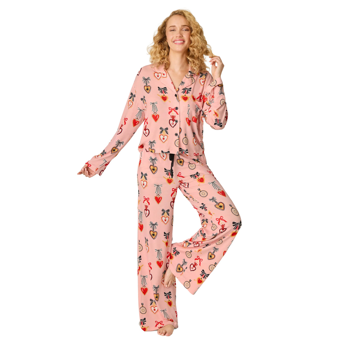 Model wearing PJ Salvage modal pyjama set in iced rose pink with colourful heart and bow print, long-sleeve button-front top and matching wide-leg pants, front view.