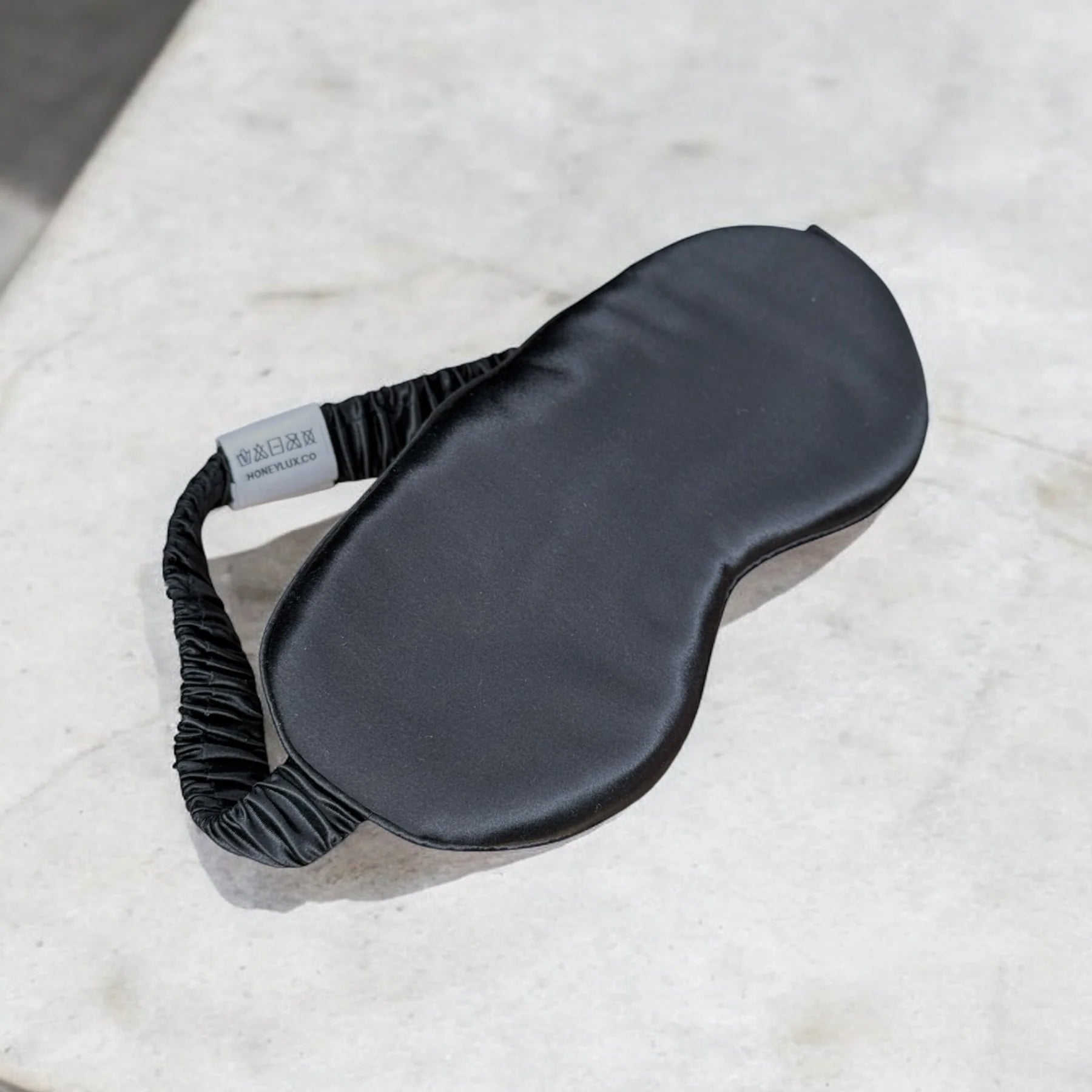 Black silk sleep mask on marble surface, angled product shot.