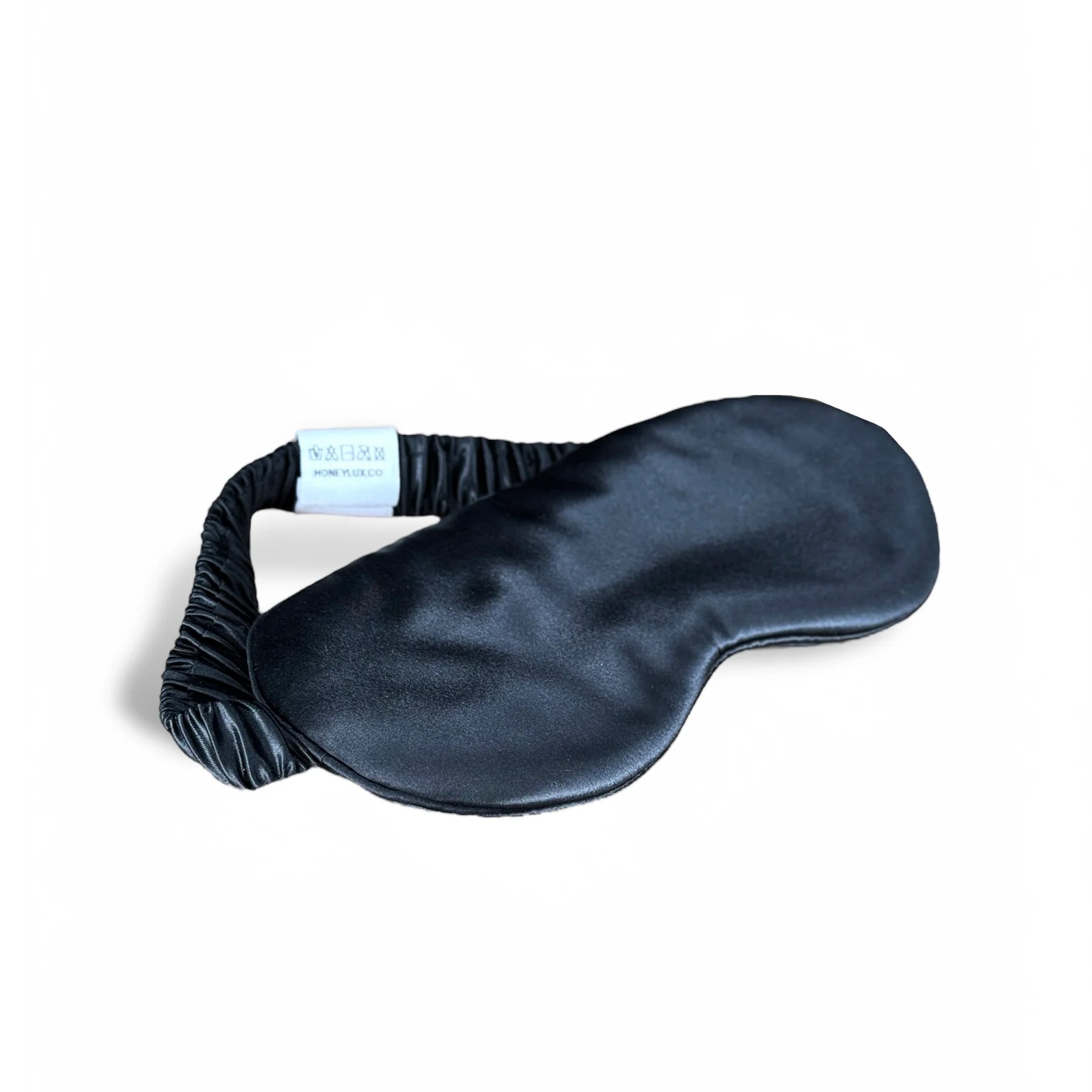 Black silk eye mask with elastic strap and brand tag, product photo.