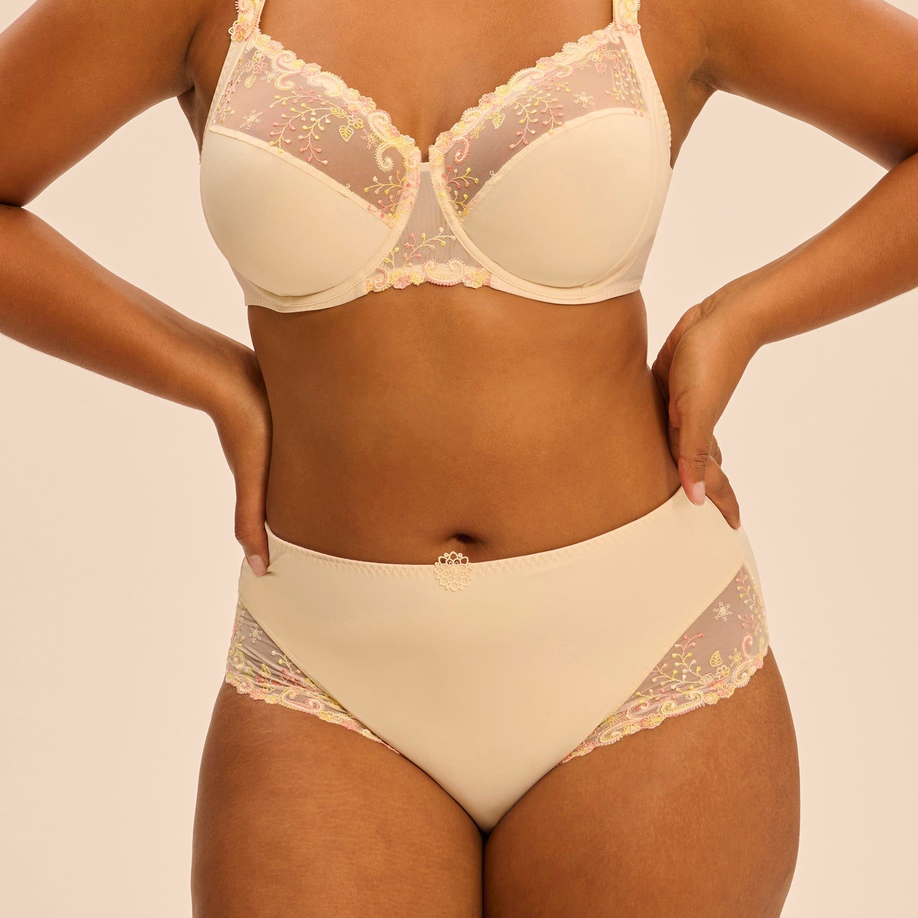 Full brief in pale yellow peach pampa with contrast coral pink embroidery at hips. Front view close up on model shown with matching 3 part full cup bra.