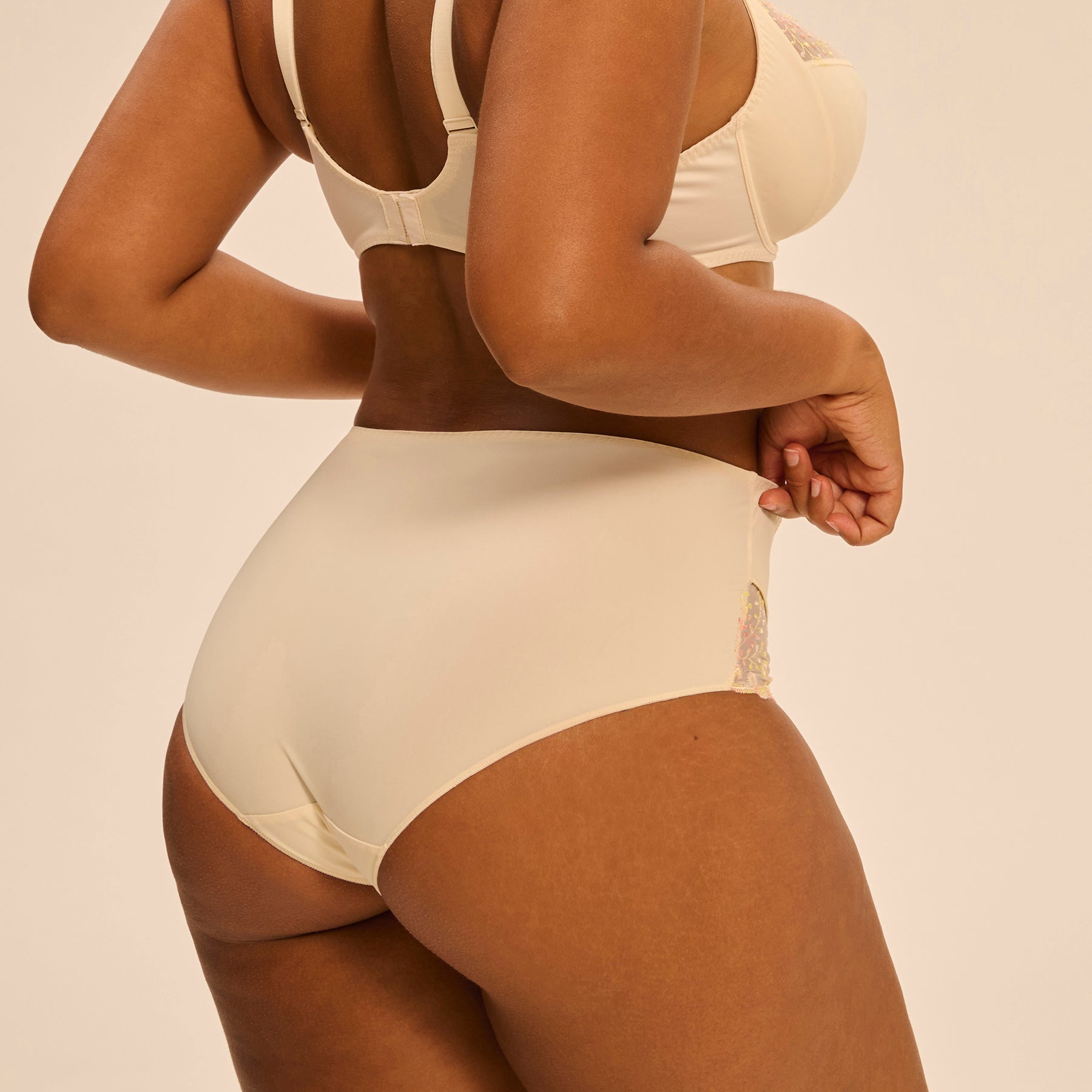 Full brief in pale yellow peach pampa with contrast coral pink embroidery at hips. Rear view close up on model shown with matching 3 part full cup bra.