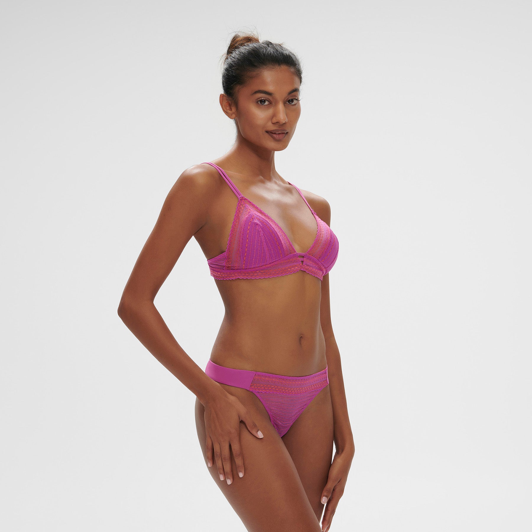 Sheer, lace wireless triangle bralette in energy pink/hot pink. Front view, on model shown with matching thong.