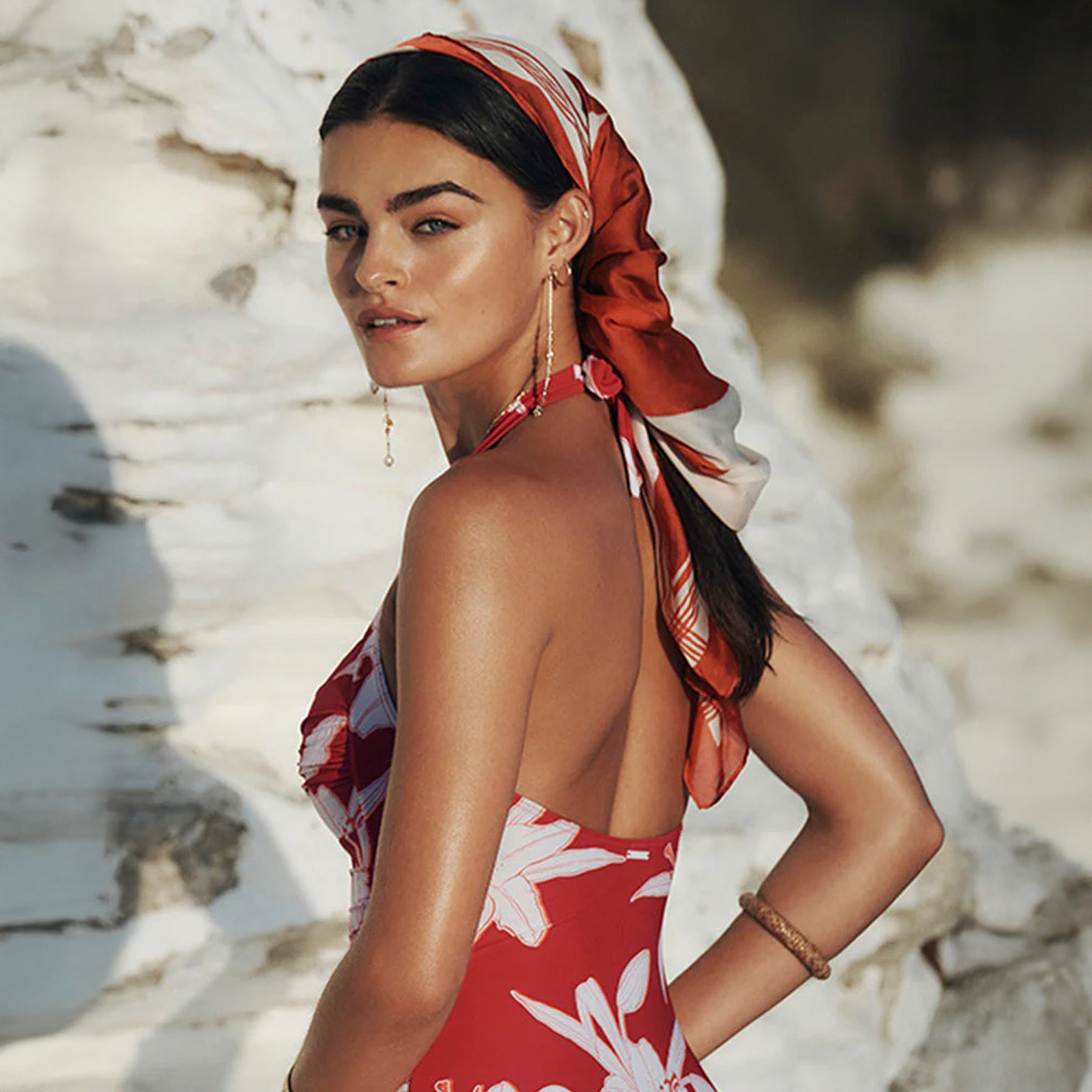 Back and side view of red floral halter swimsuit with open back and neck tie, styled with matching red headscarf.