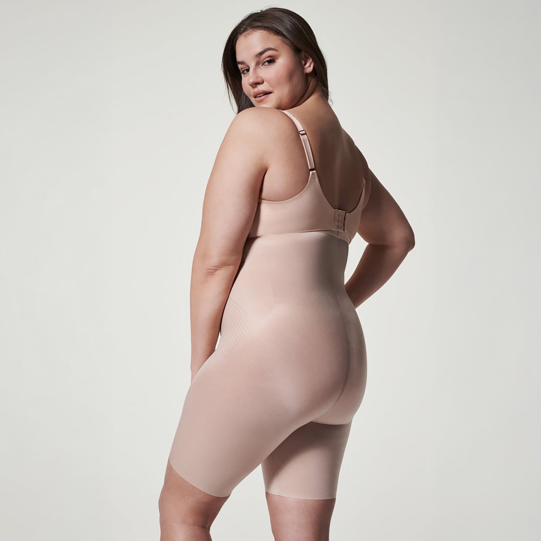 Model wearing SPANX High-Waist Control Short Mid-Thigh in Champagne Beige, designed to smooth waistline and thighs under clothing.
