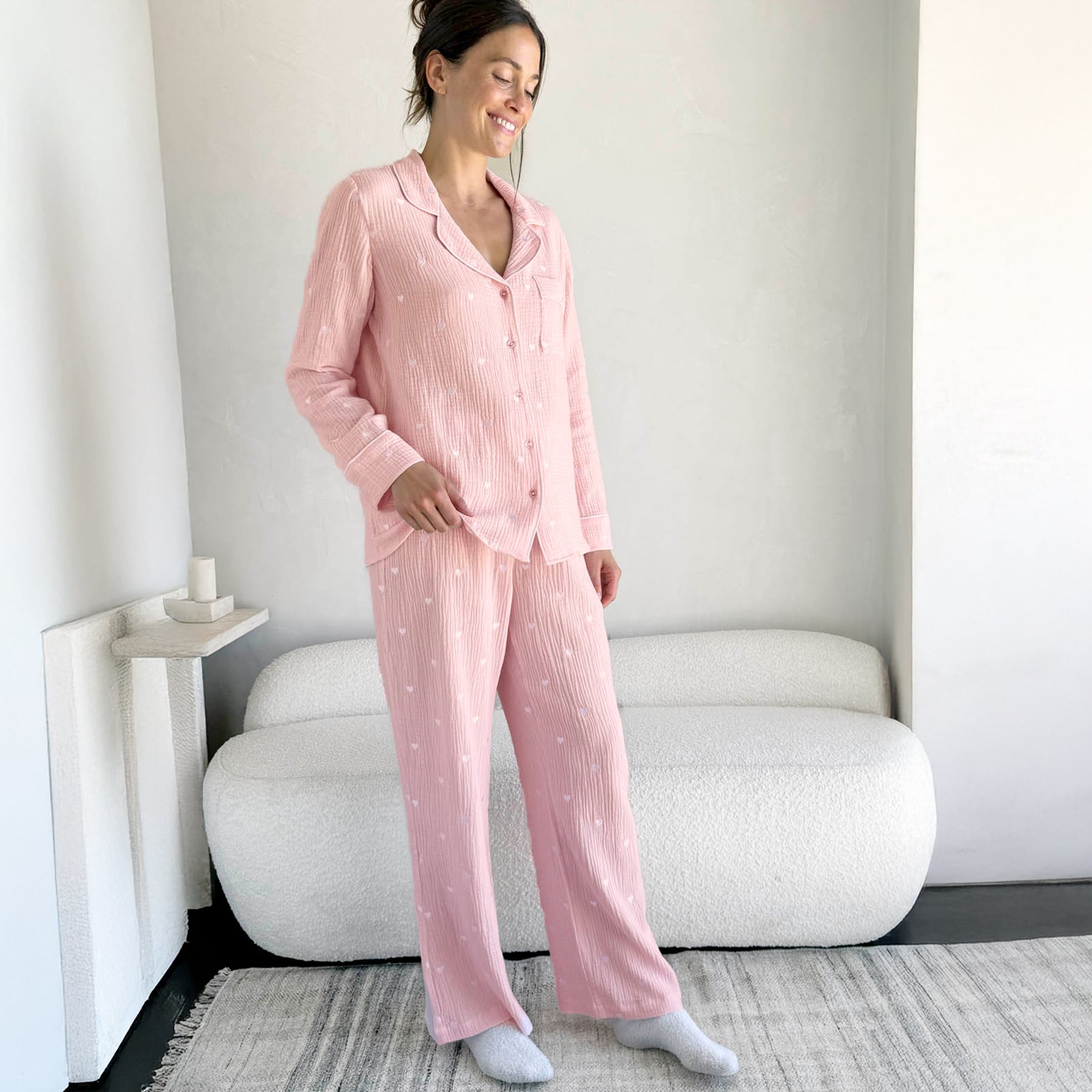 classic button up pyjama set in crinkle cotton in baby pink with mini white embroidered hearts. Matching white  contrast piping on trims. Front/side view on model.