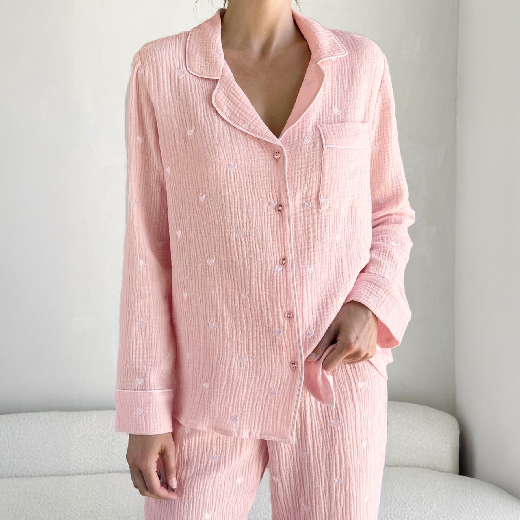 classic button up pyjama set in crinkle cotton in baby pink with mini white embroidered hearts. Matching white  contrast piping on trims. Front view close up on model.