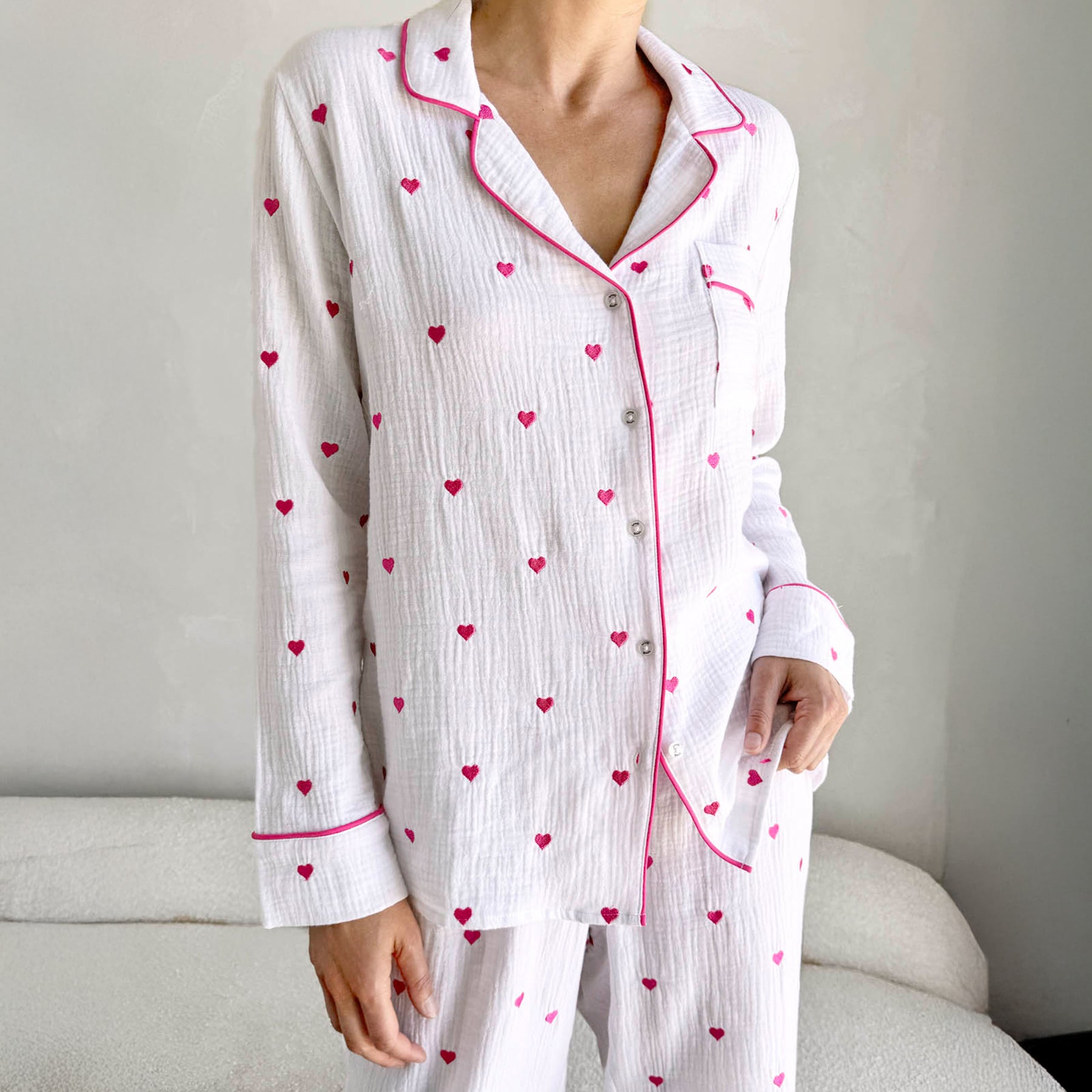 classic button up pyjama set in crinkle cotton in white with mini hot pink embroidered hearts. Matching hot pink contrast piping on trims. Front view close up on model.