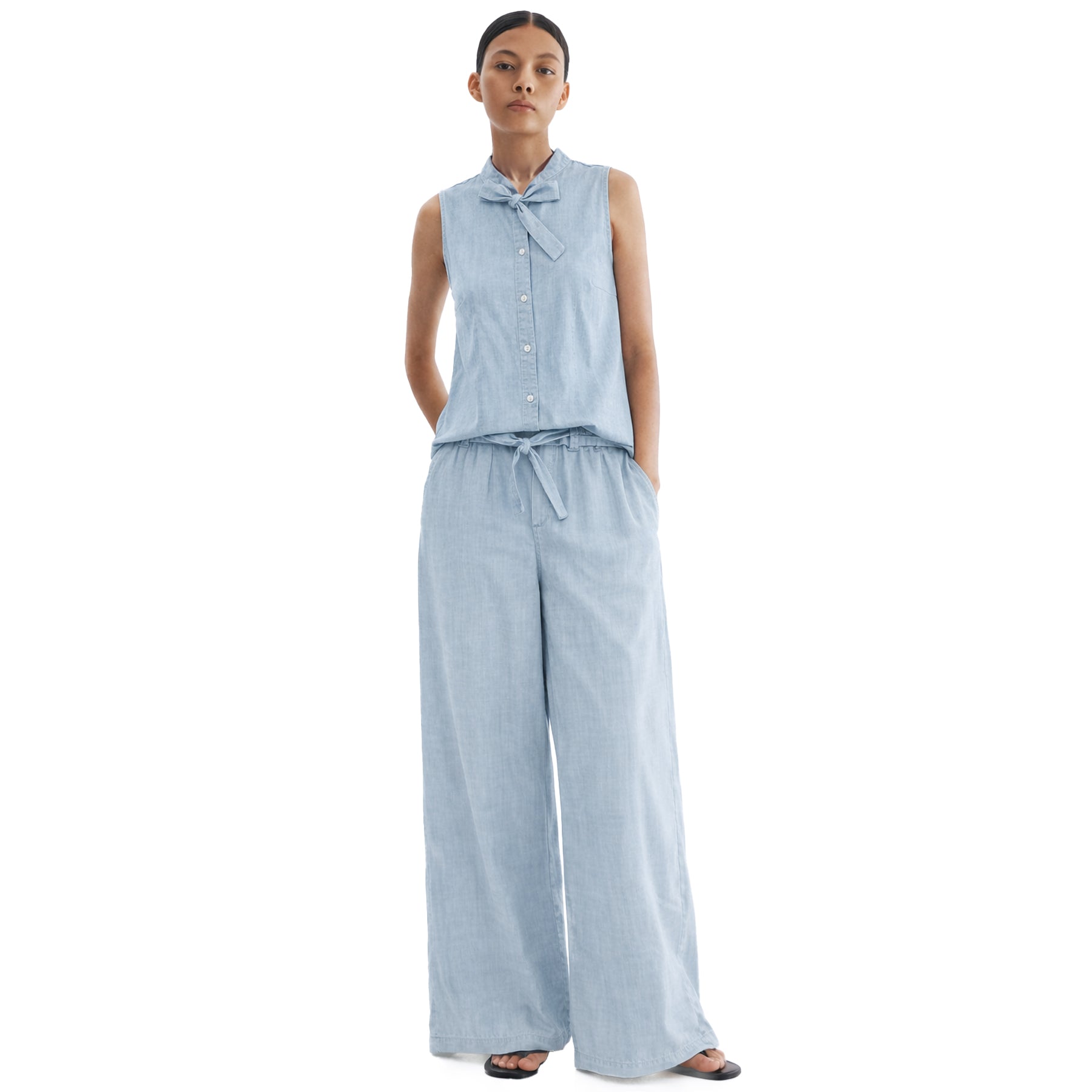 Model wearing light blue sleeveless chambray blouse with bow tie detail, styled with matching wide-leg pants for a relaxed, coordinated look.