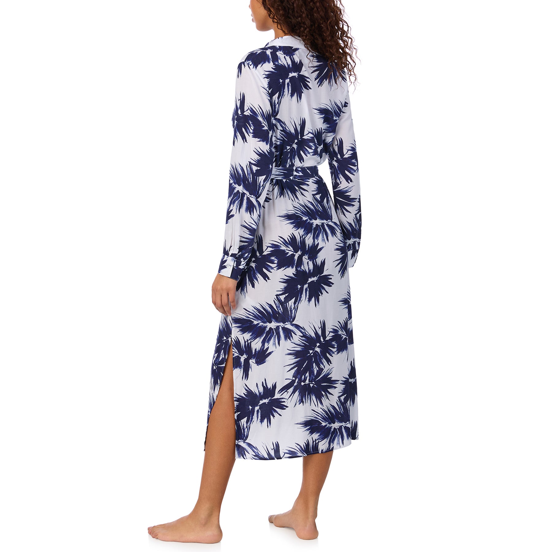 Back view of model wearing a long-sleeve, button-down shirt dress with navy palm print and side slit detail.