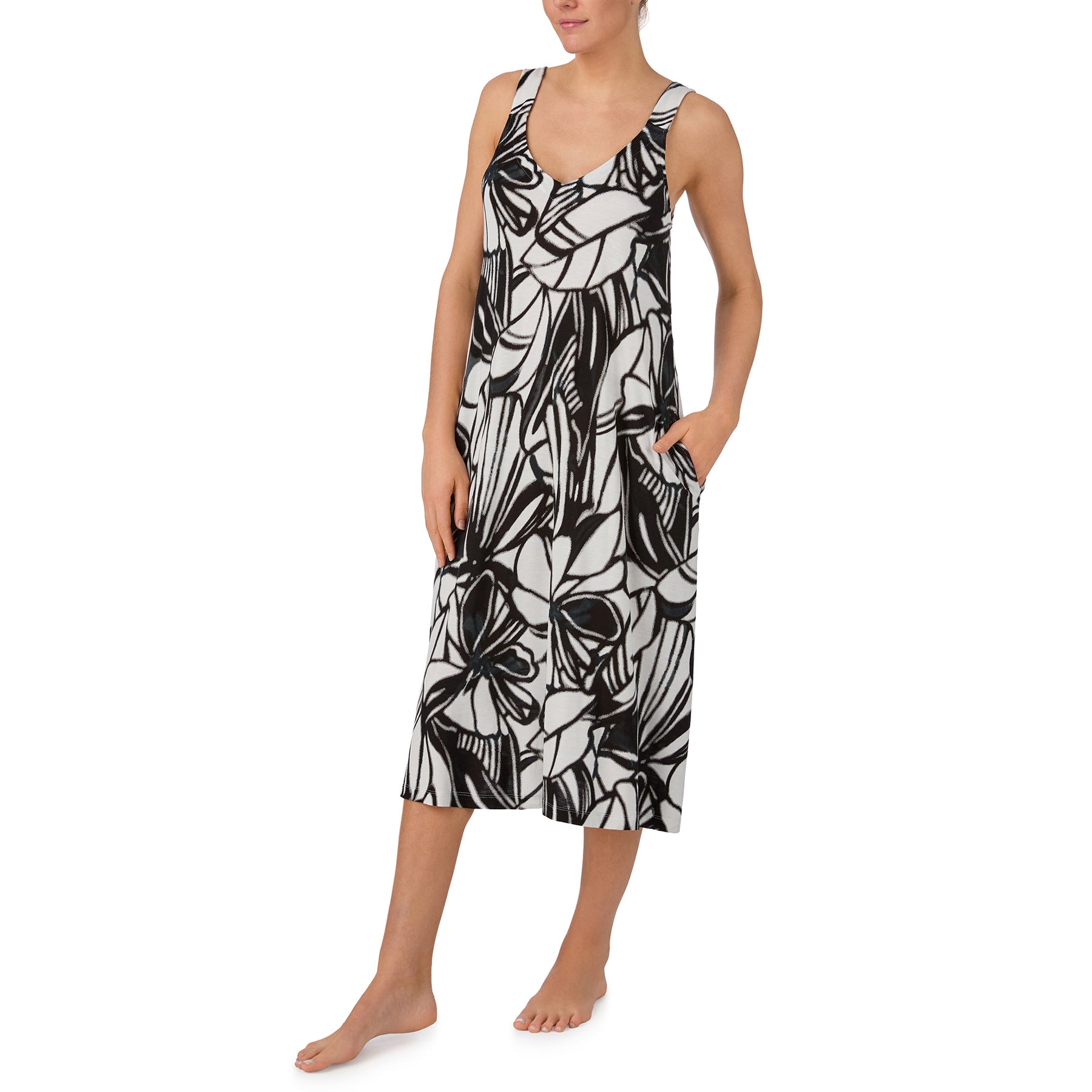 Woman wearing a black and white abstract floral sleep dress with side pockets and lightweight draped fabric.