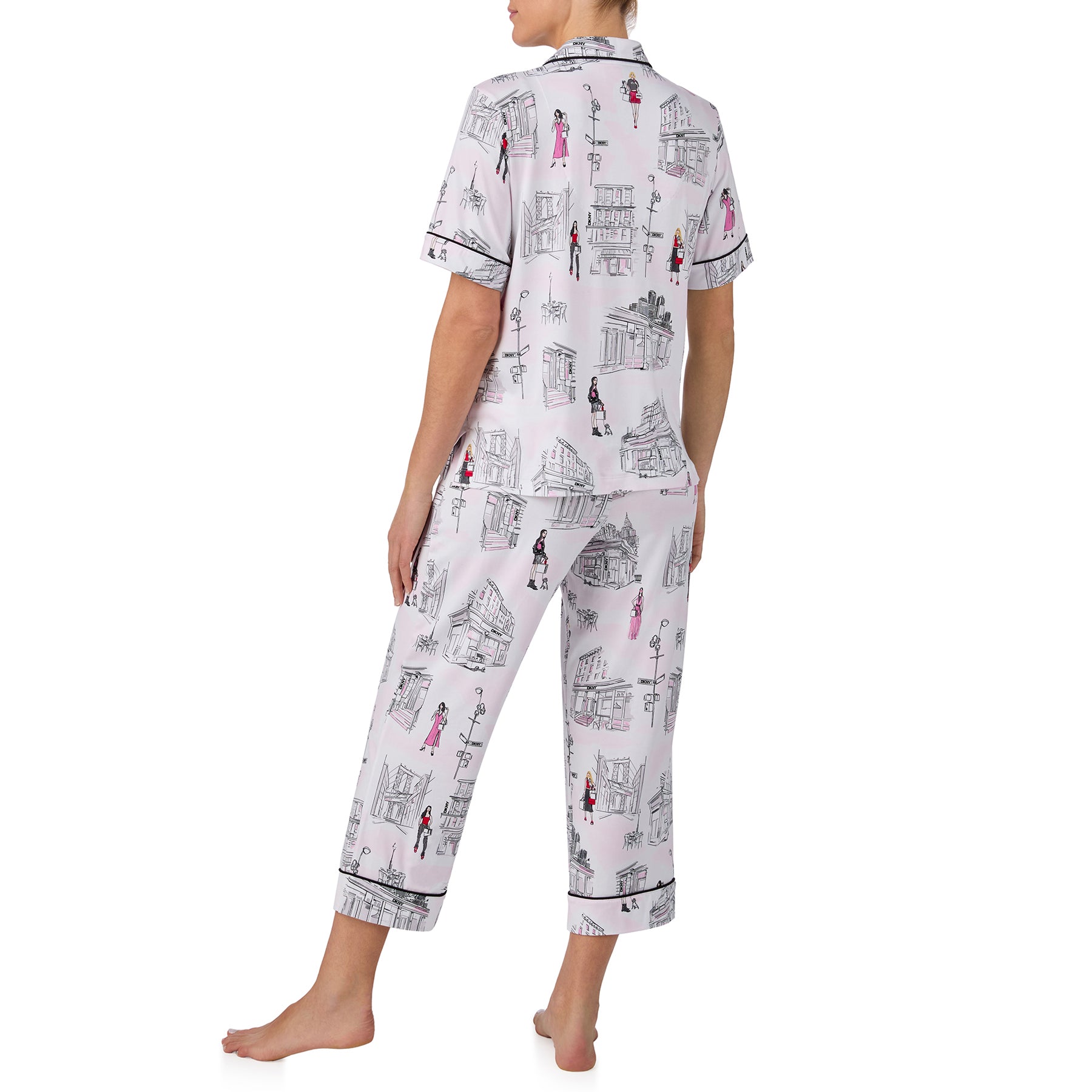Back view of a soft white pyjama set with black piping trim, relaxed cropped pants, and a whimsical cityscape print with feminine pink accents.