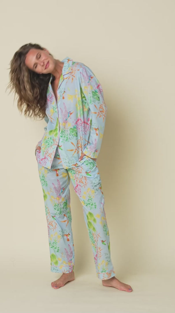 long sleeve button up pajamas with matching long pants in a multicolour hummingbird print on a blue background. Model shown turning around to view all angles.