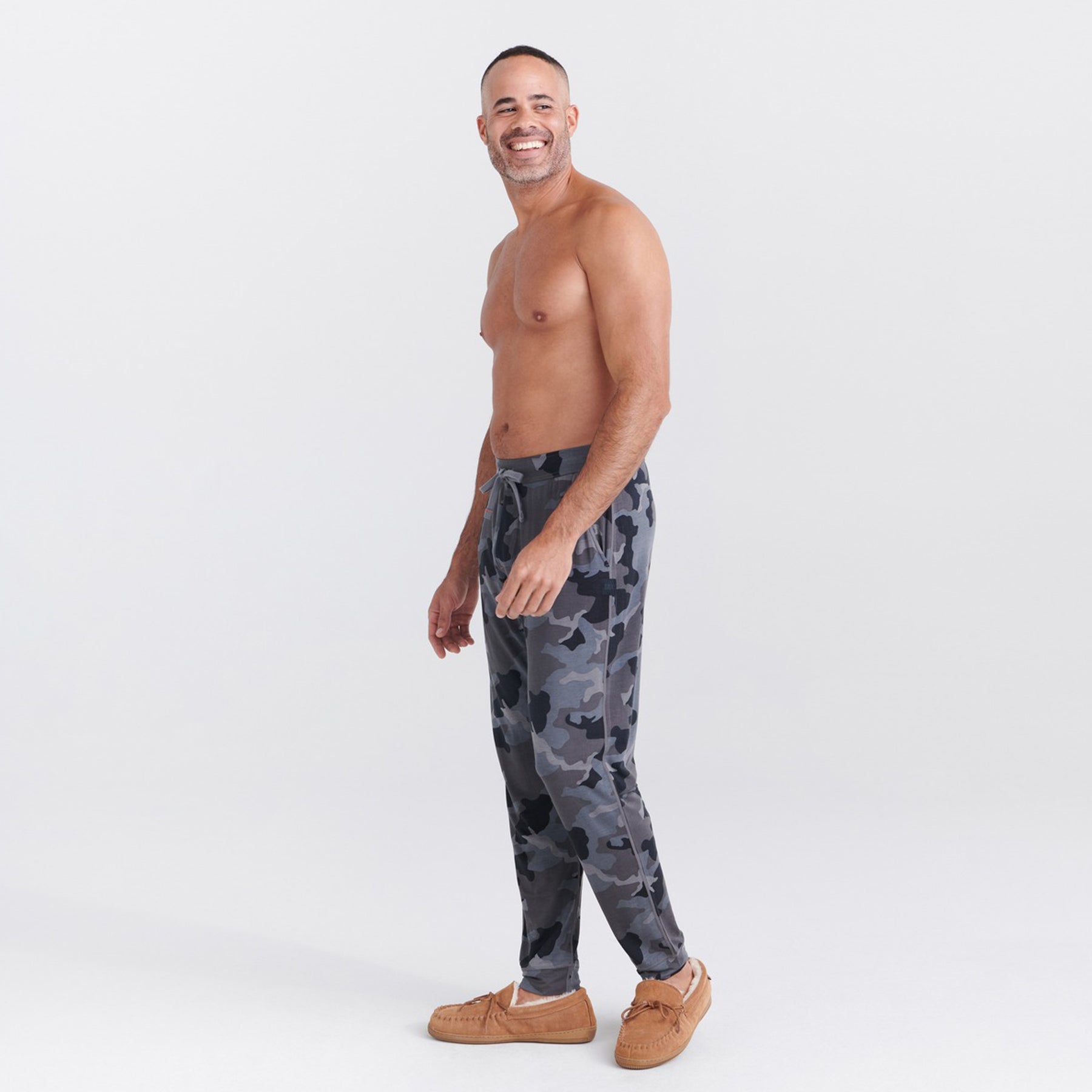 Dark camouflage print lounge pants styled with slippers, shown in profile.